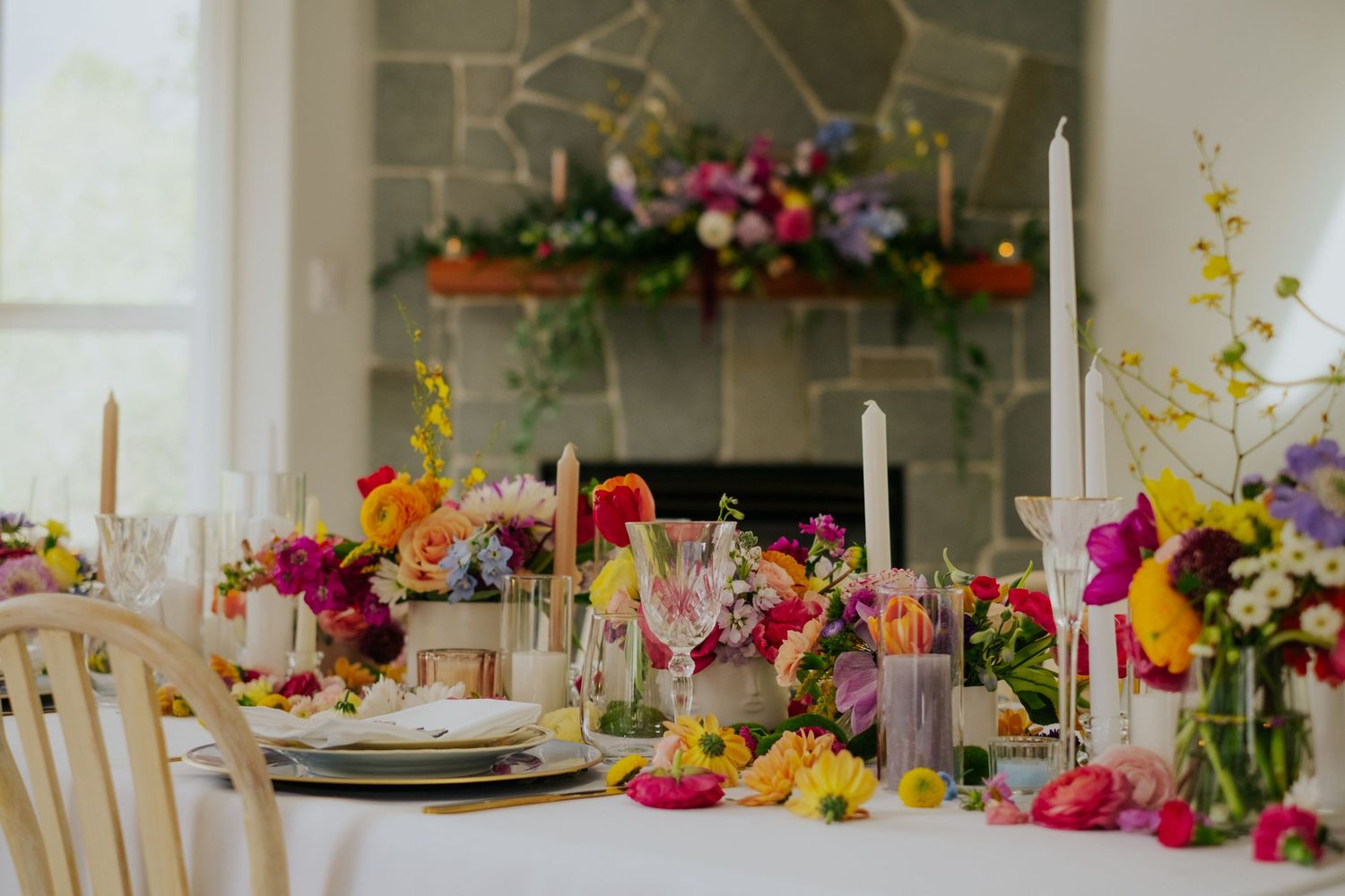 Elegant wedding reception table adorned with vibrant multicolored flowers, tall candles, and decorative glassware.