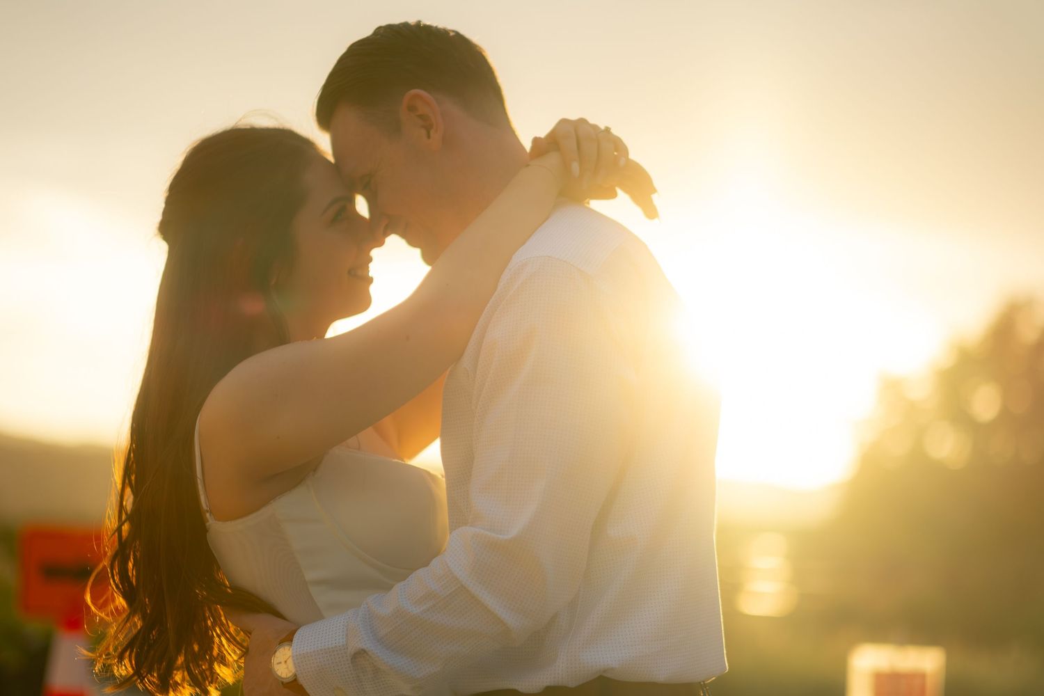 A couple embraces tenderly in warm golden sunset light during their engagement shoot.