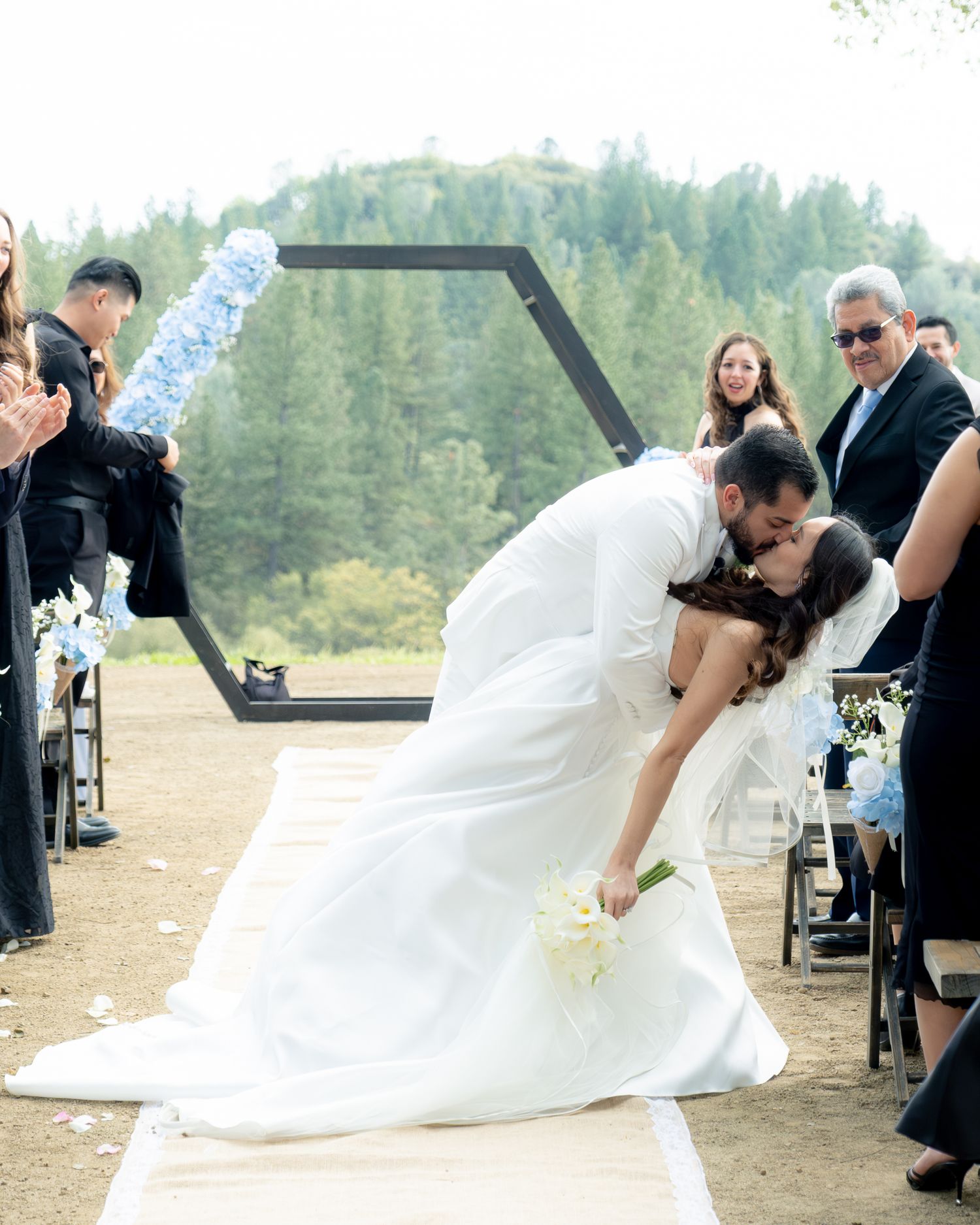 Bride and groom share romantic dip kiss at outdoor wedding ceremony with hexagonal arch backdrop.