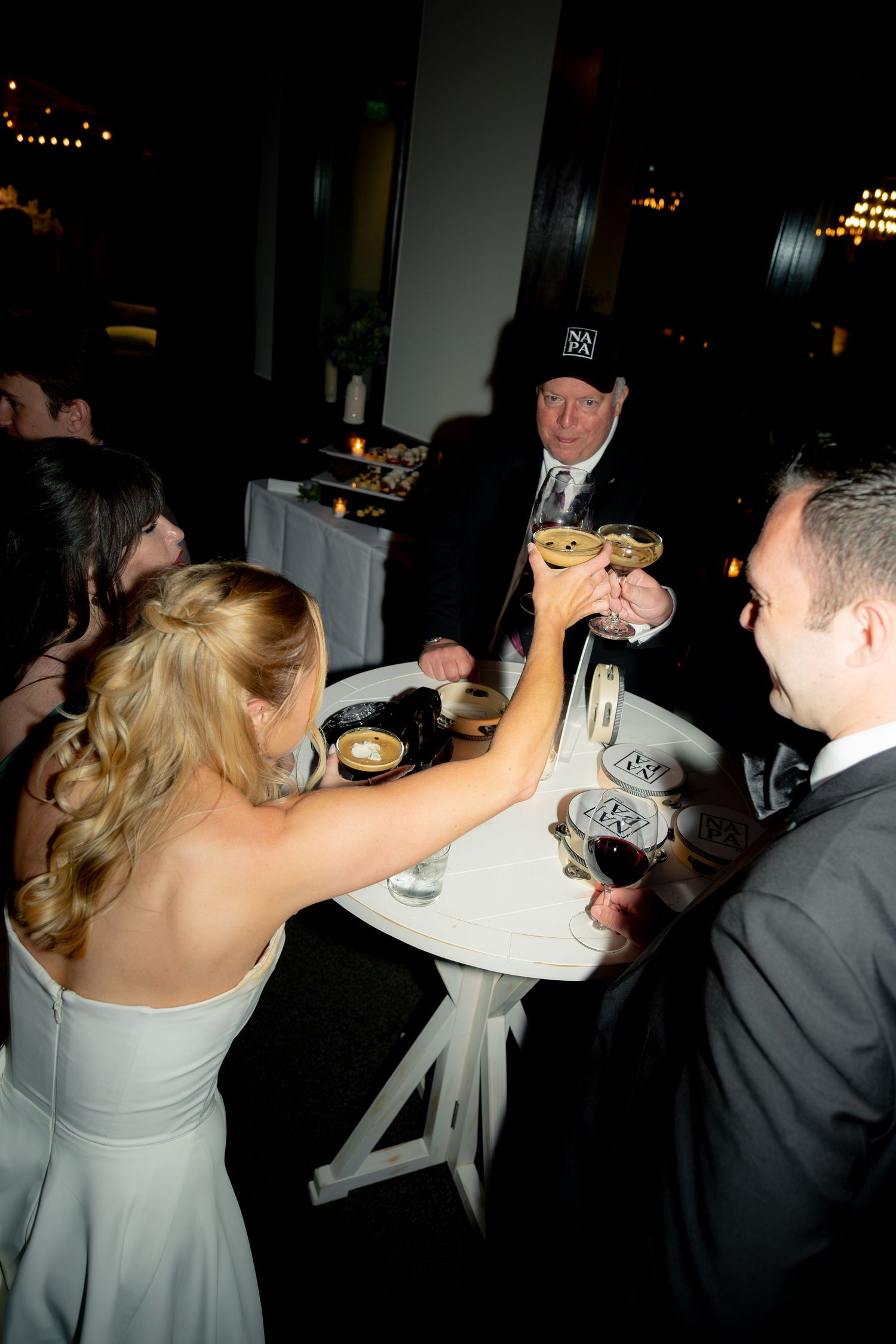 Bride in white gown toasts champagne glasses with groom and elderly guest at wedding reception.