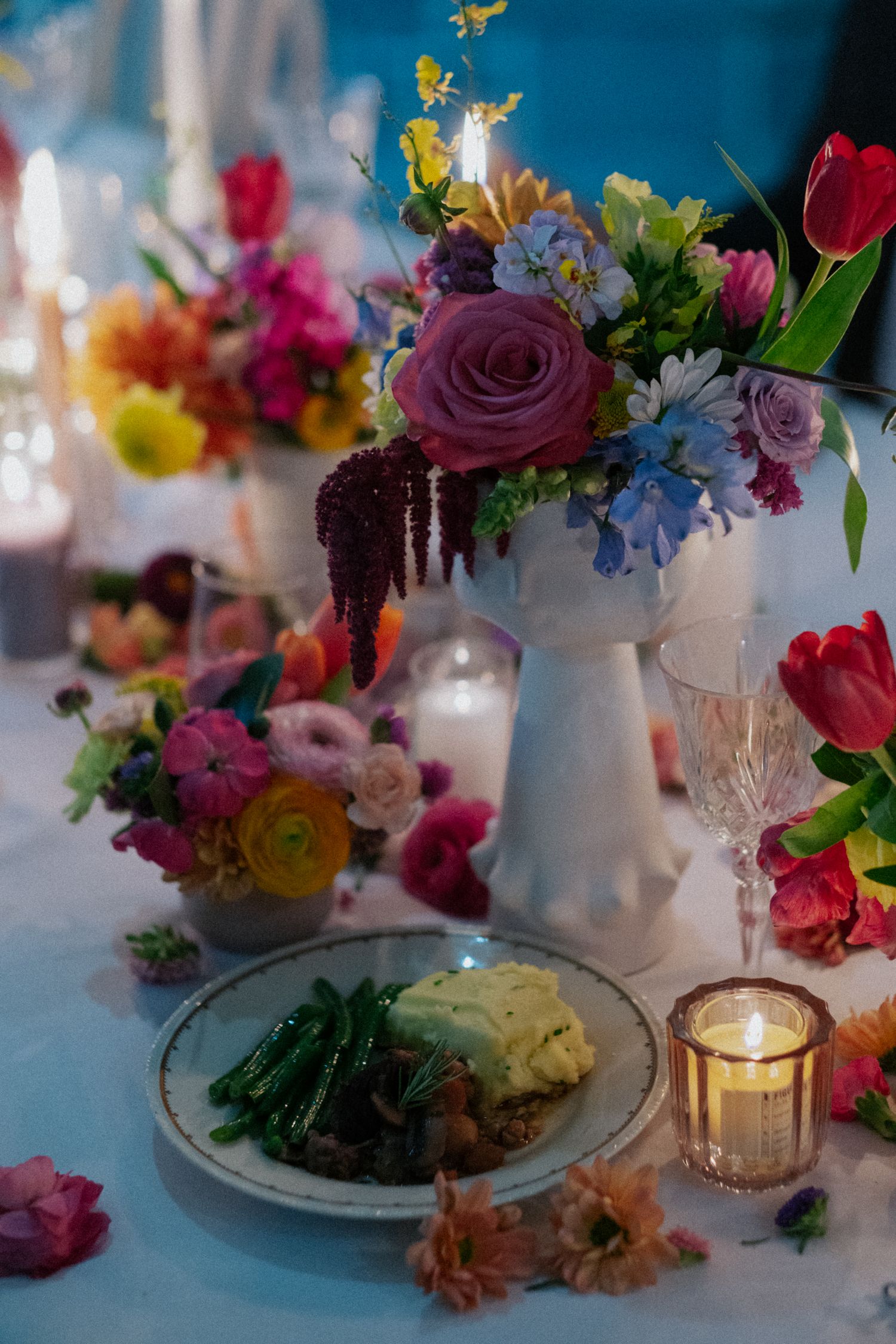 Elegant wedding table with colorful floral arrangements, candles, and plated dinner service at reception.