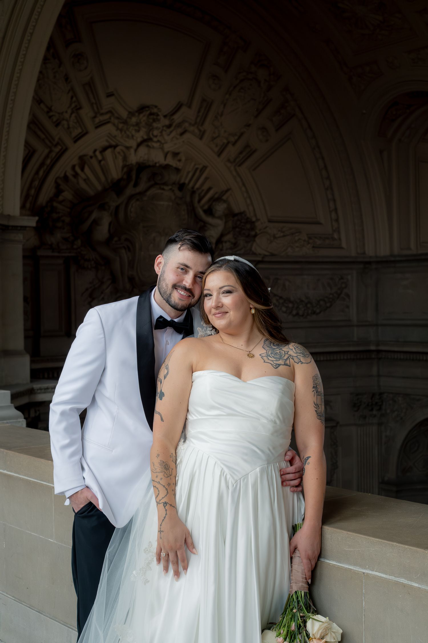Bride and groom posing in wedding attire inside elegant architectural venue.