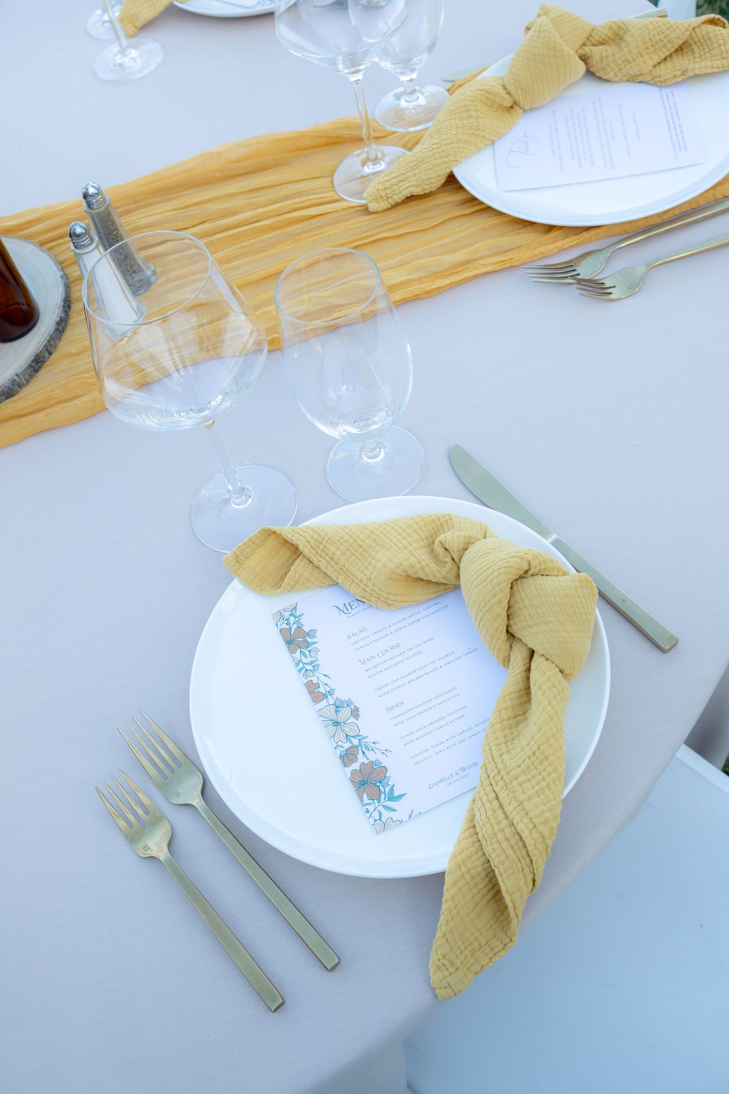 Elegant wedding reception place setting with gold napkin, white plate, menu card, and crystal glasses.