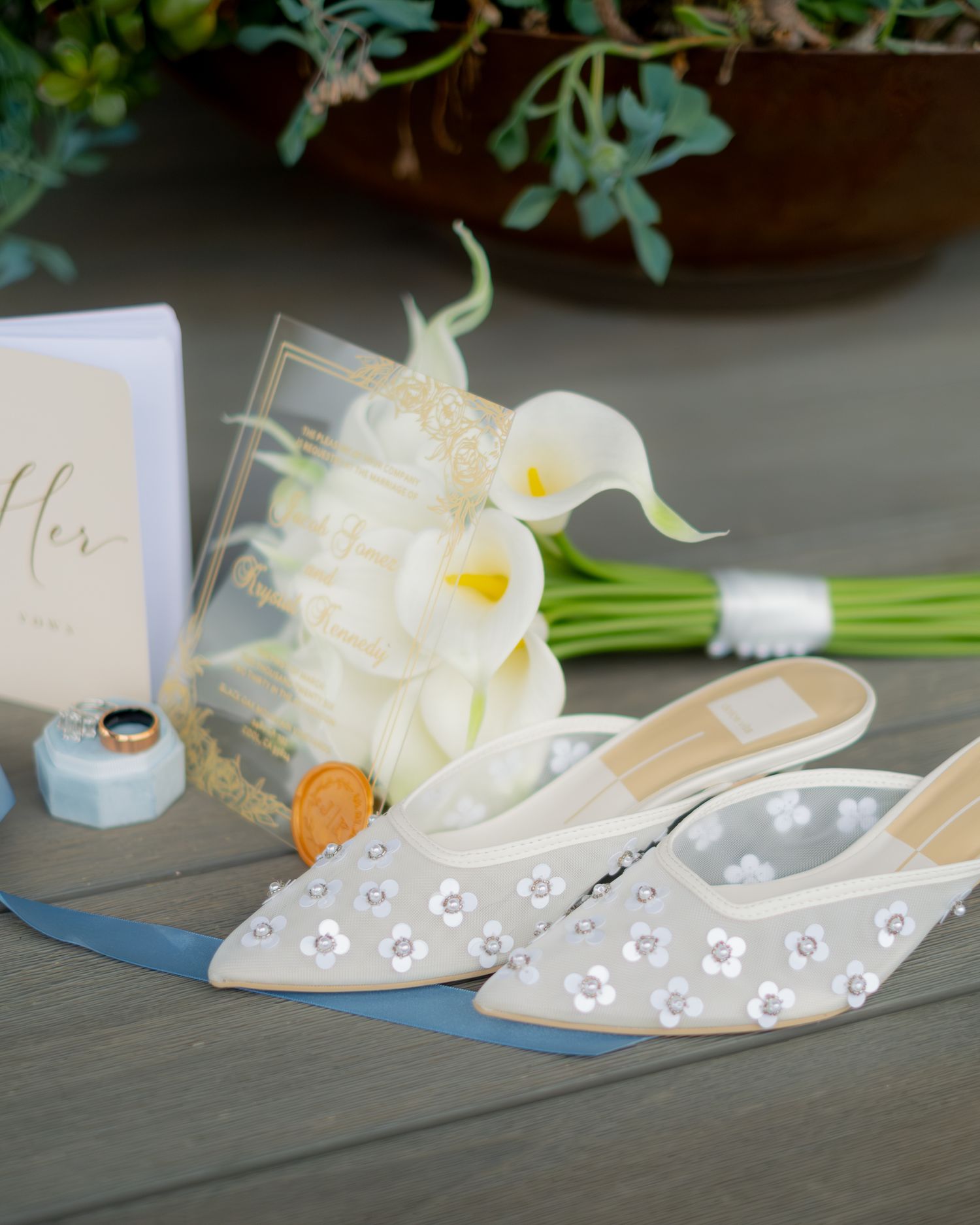 Elegant wedding flat shoes with floral embellishments beside a white calla lily bouquet and bridal accessories.
