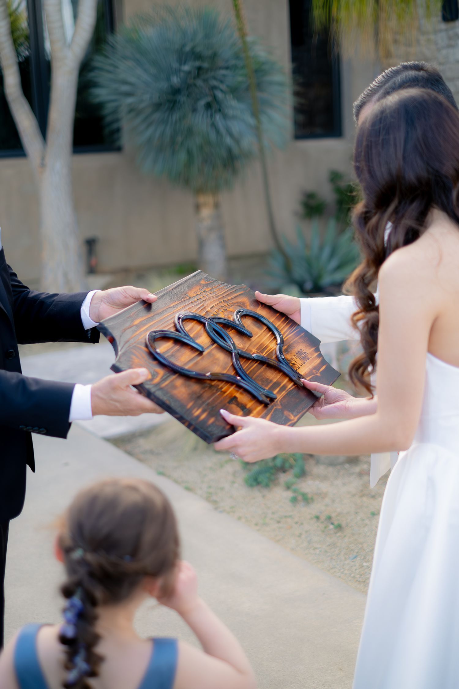 Bride and groom hold a rustic wooden sign with metal letters during an outdoor wedding ceremony.