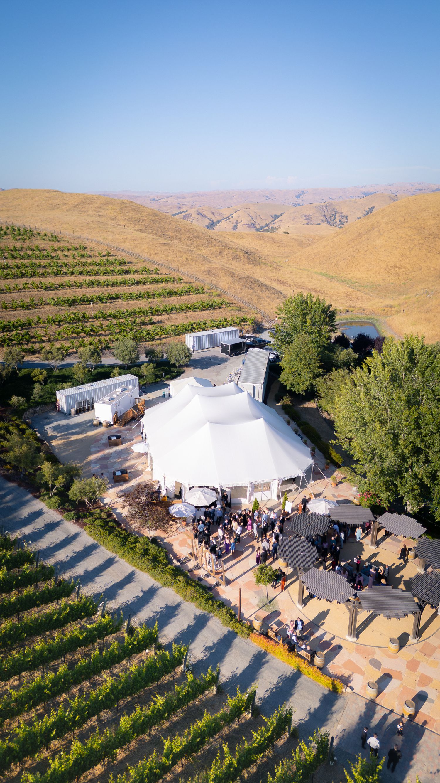Aerial view of a vineyard wedding venue with white tent reception area surrounded by rolling hills.