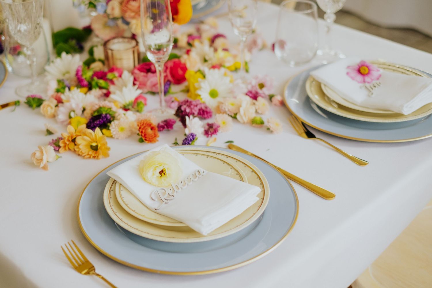 Elegant wedding table setting with gold cutlery, blue and gold plates, and vibrant floral centerpiece.
