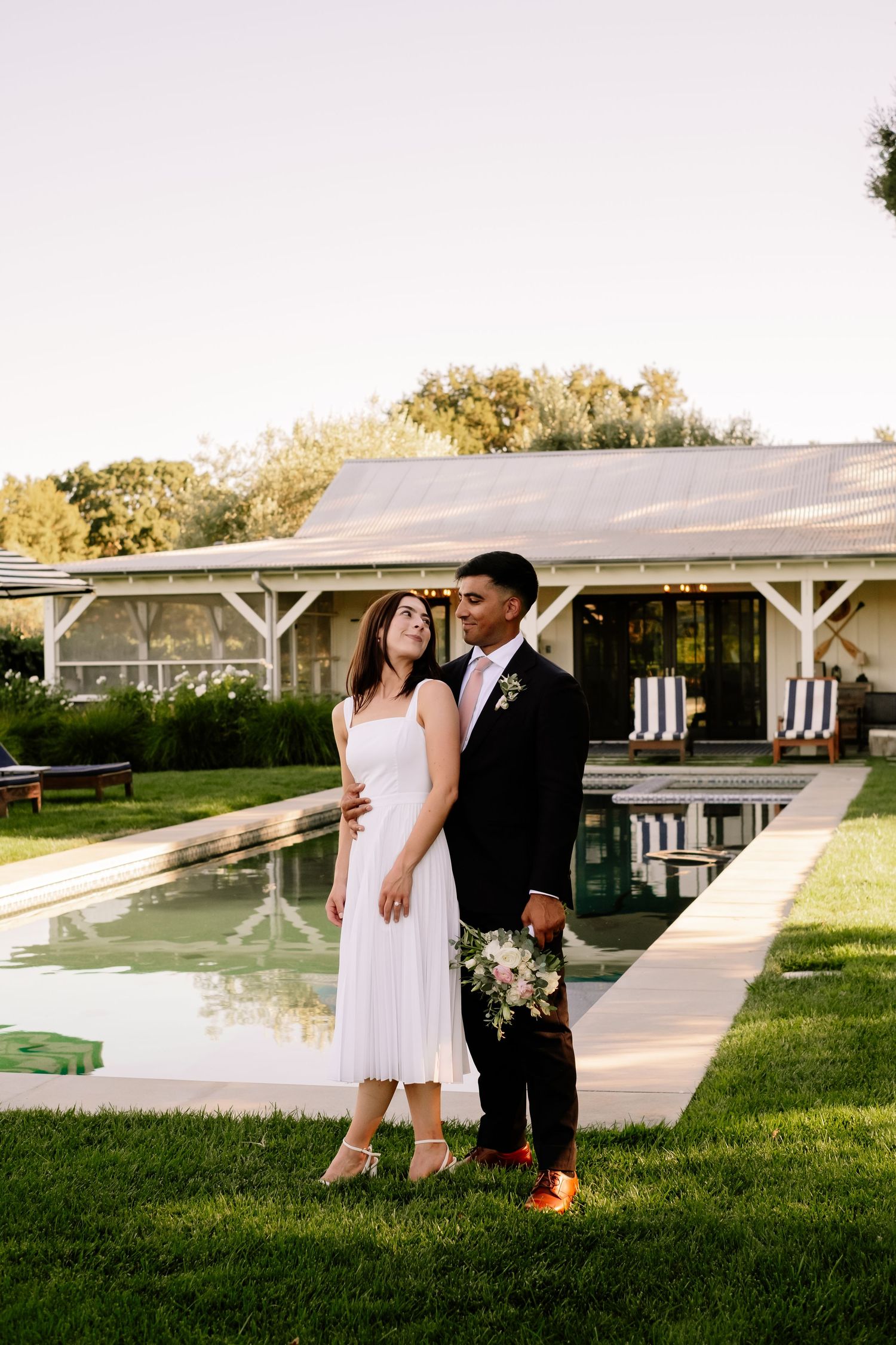Bride and groom embracing near a pool at golden hour on wedding day.