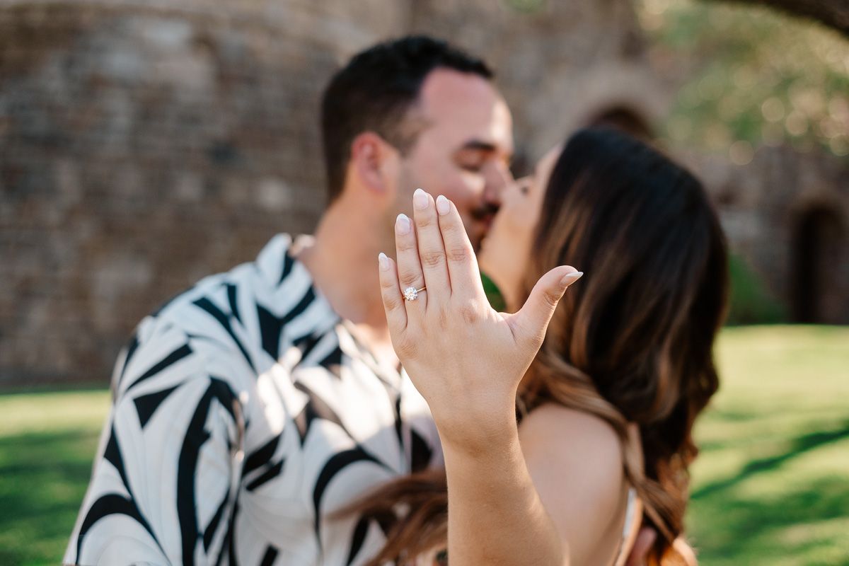 Newly engaged couple kissing as woman displays diamond engagement ring toward camera.