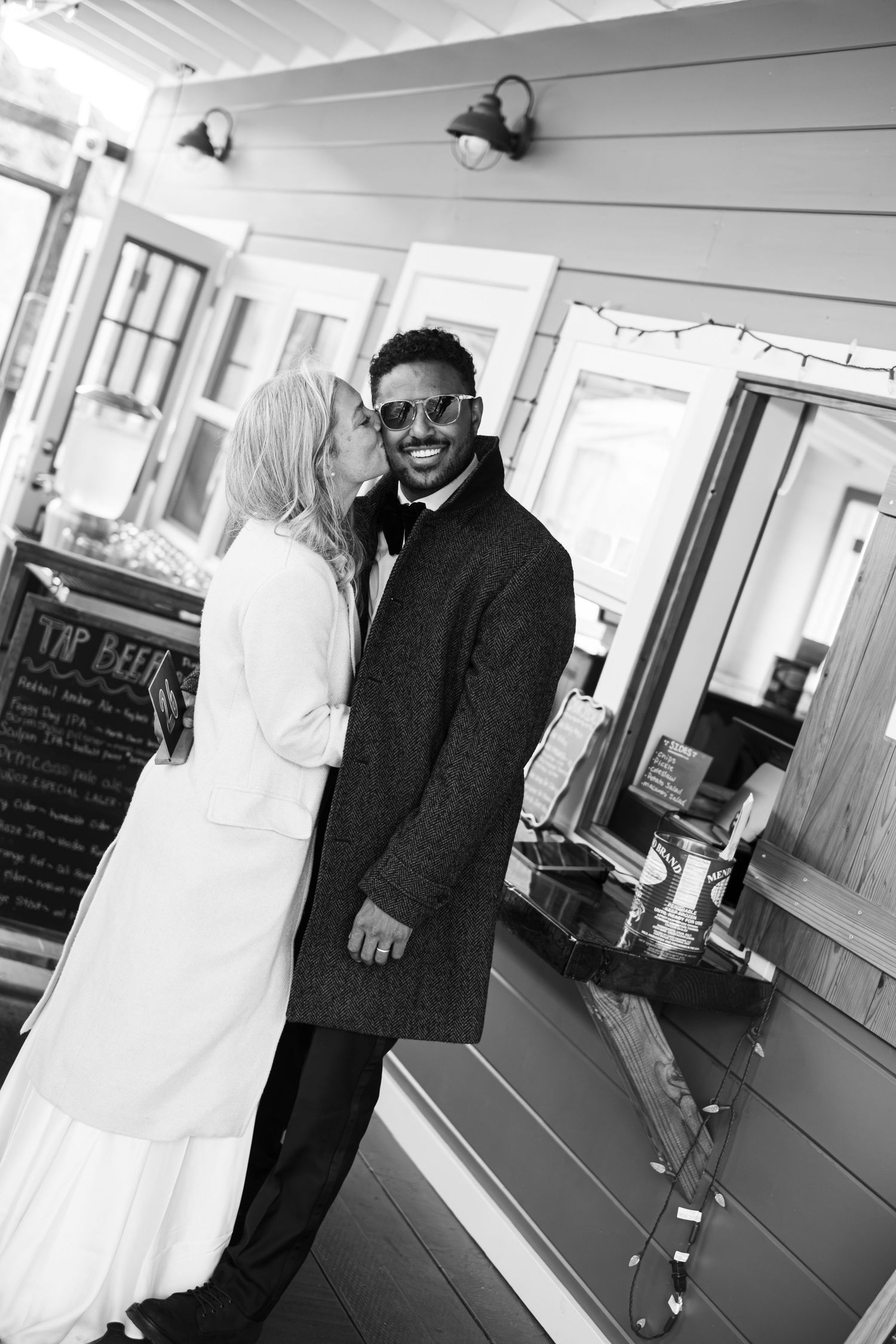 Black and white photo of a bride kissing her groom on the cheek at a bar venue.
