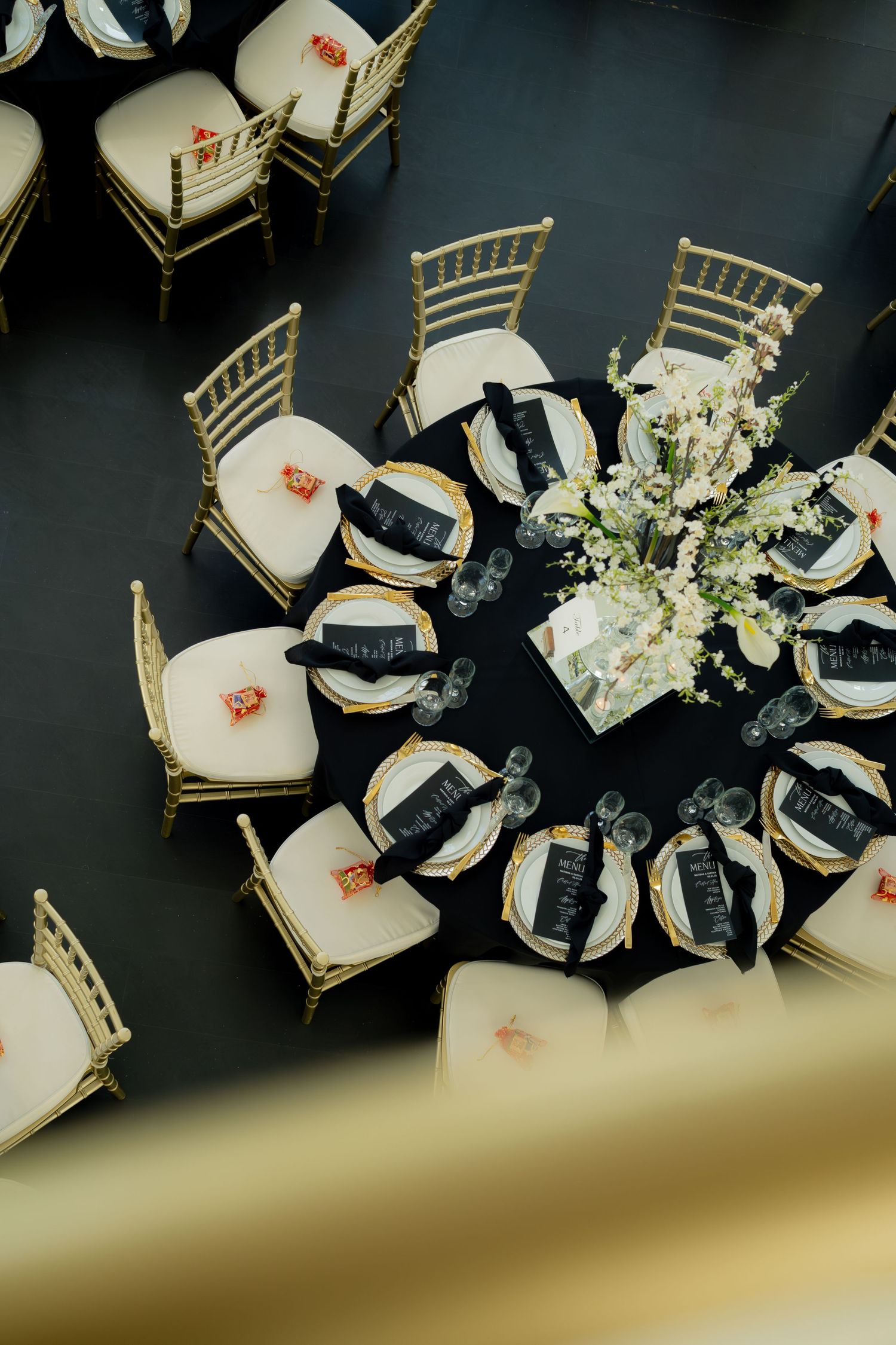 Aerial view of elegant black and gold wedding reception tables with floral centerpieces and gold chiavari chairs.