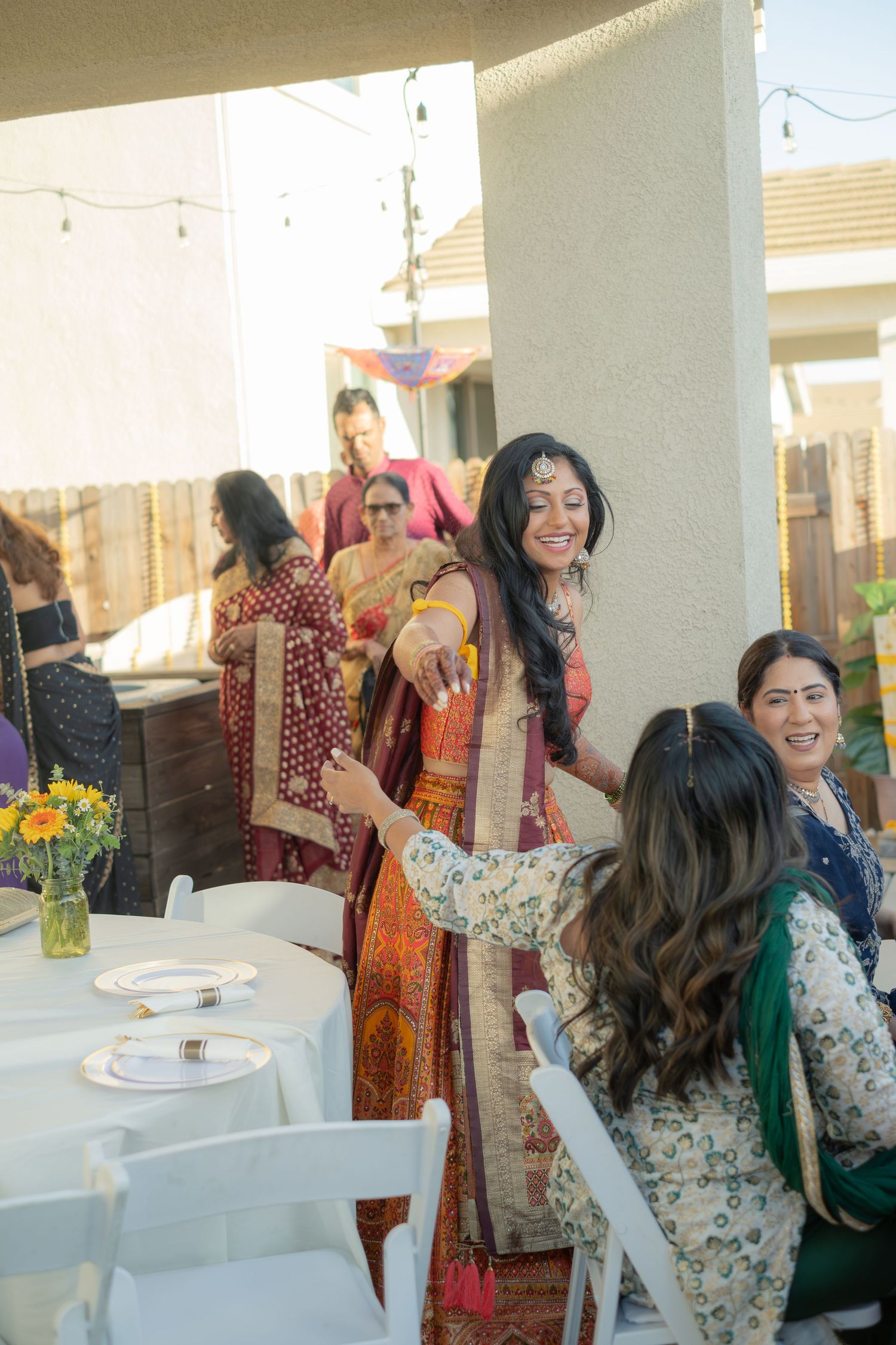 Indian bride in colorful lehenga laughing during outdoor pre-wedding haldi ceremony with guests.