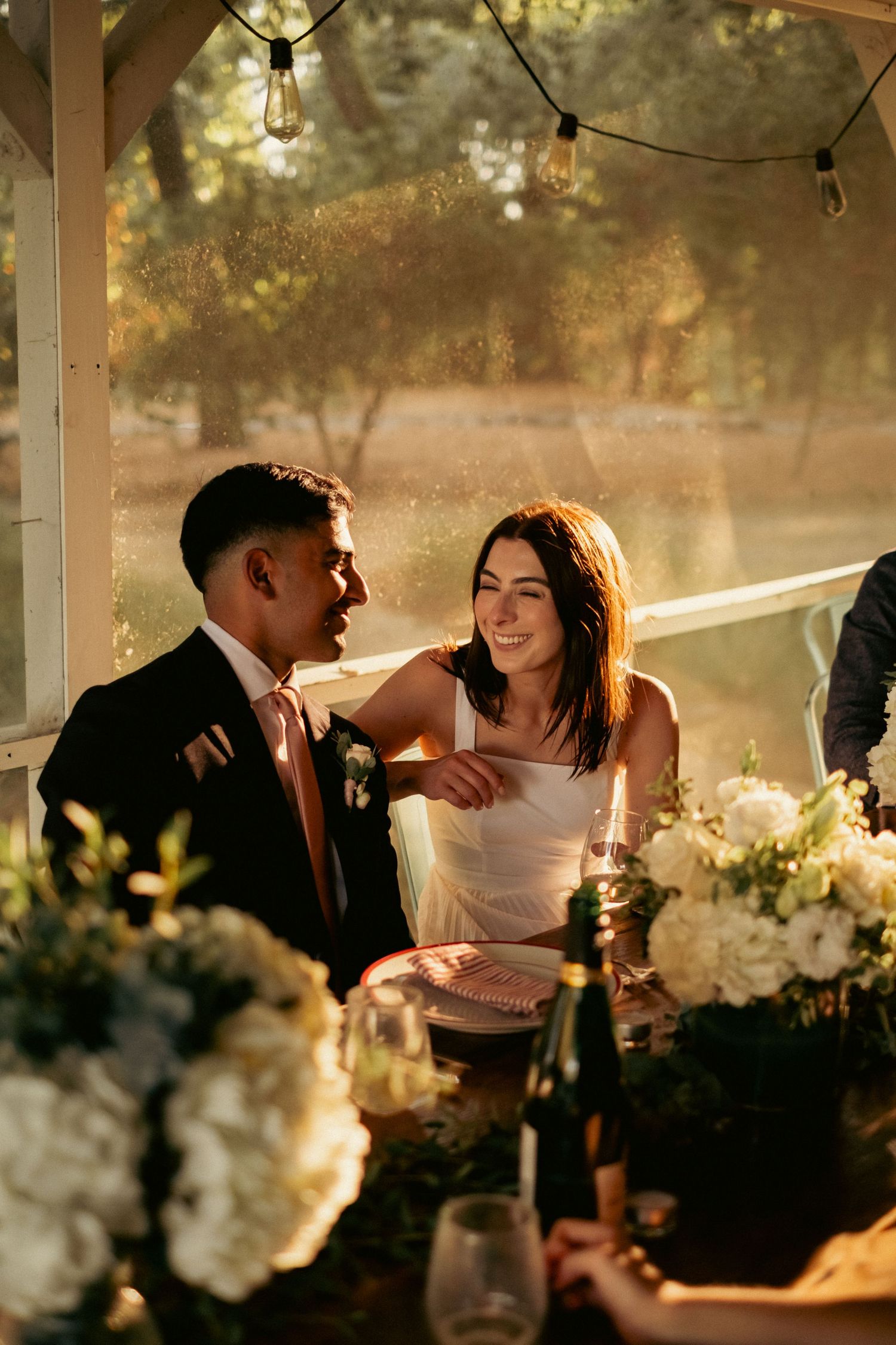 Smiling bride in white dress and groom in navy suit at candlelit wedding reception table.