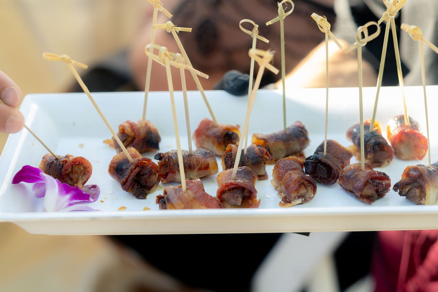 Server presenting a platter of bacon-wrapped appetizers with toothpicks at a wedding reception.