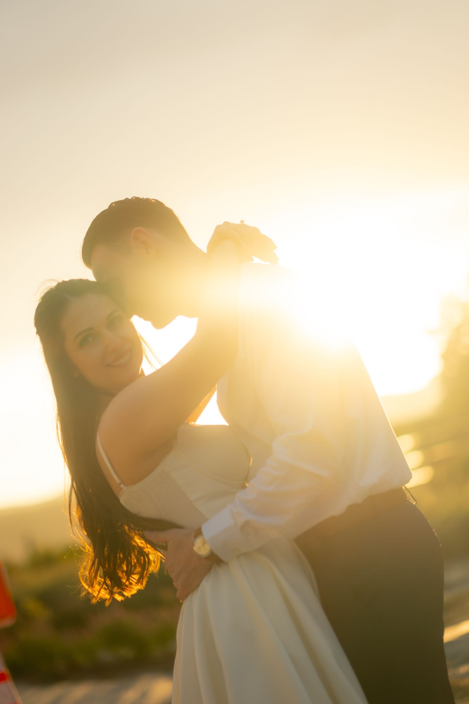 Romantic couple embracing in warm golden sunset light, bride smiling joyfully.