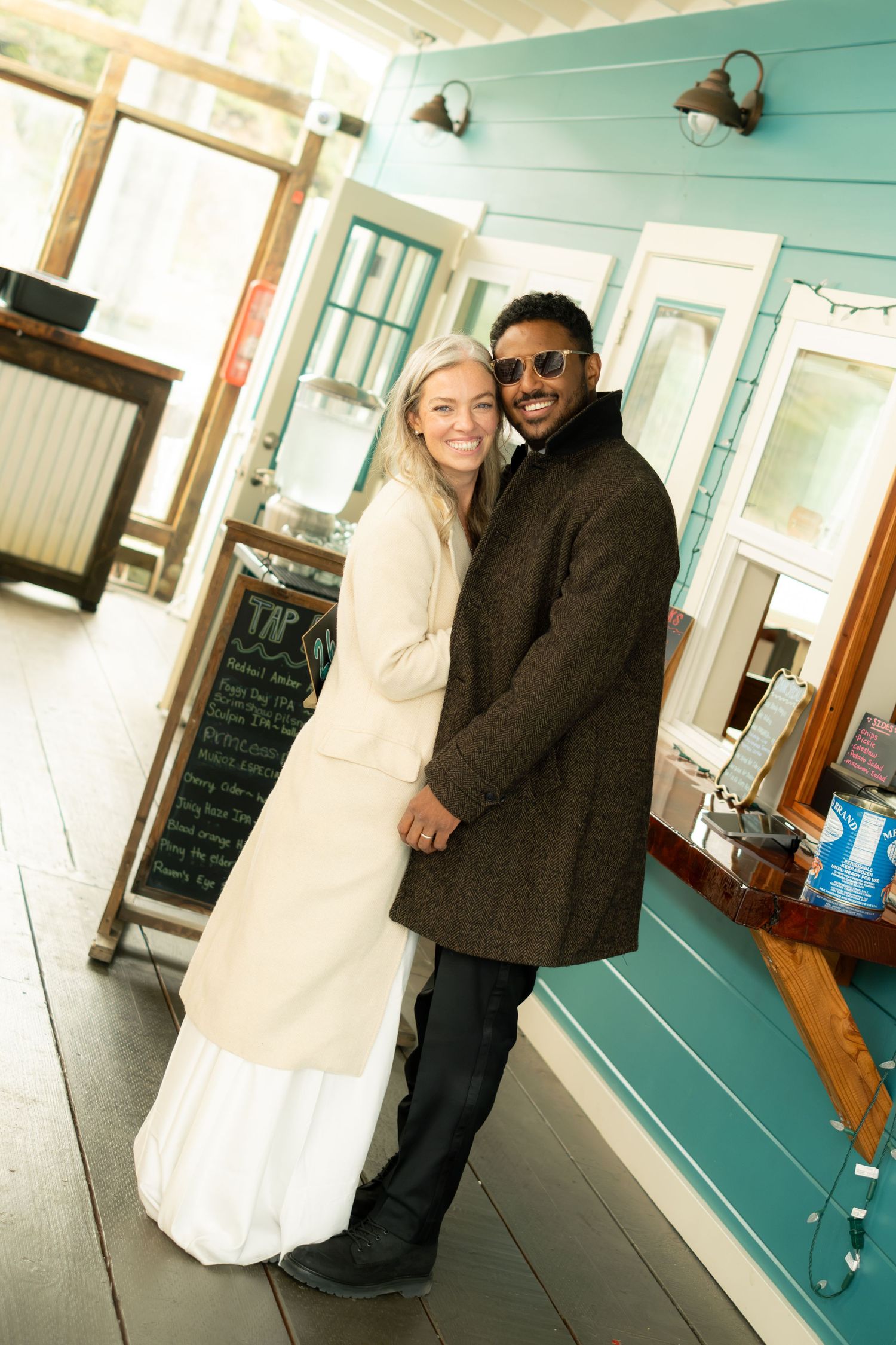 Bride and groom embracing inside a charming teal coastal cafe on their wedding day.