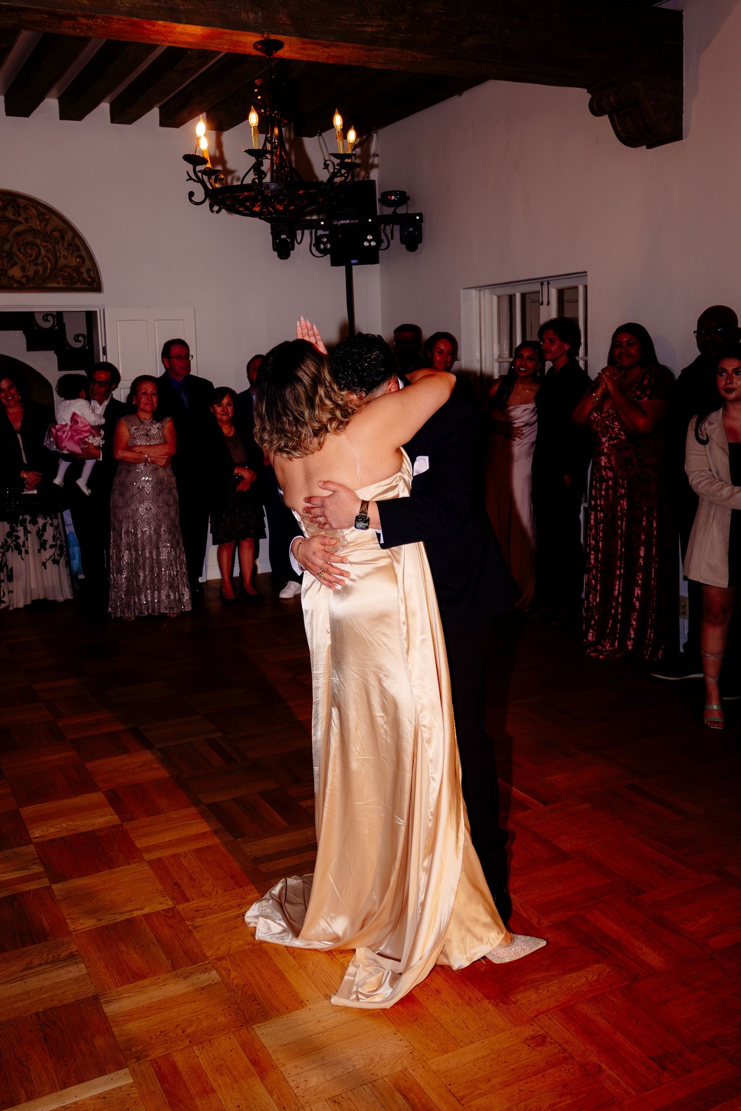 Bride and groom share intimate first dance embrace in warmly lit reception hall.