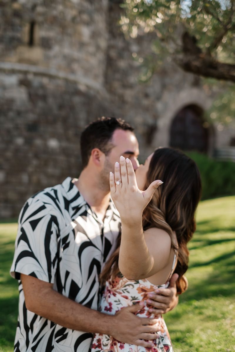 Newly engaged couple kissing while woman shows off her engagement ring to camera.