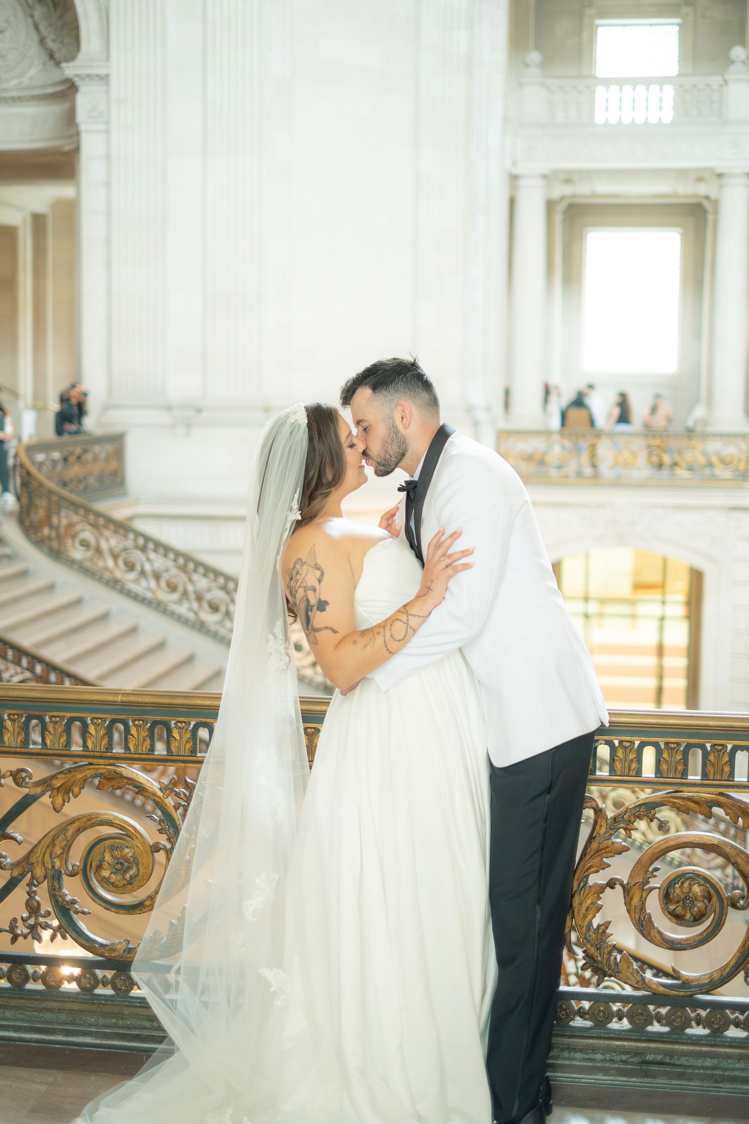 Bride and groom share a romantic kiss on the grand staircase balcony of San Francisco City Hall.