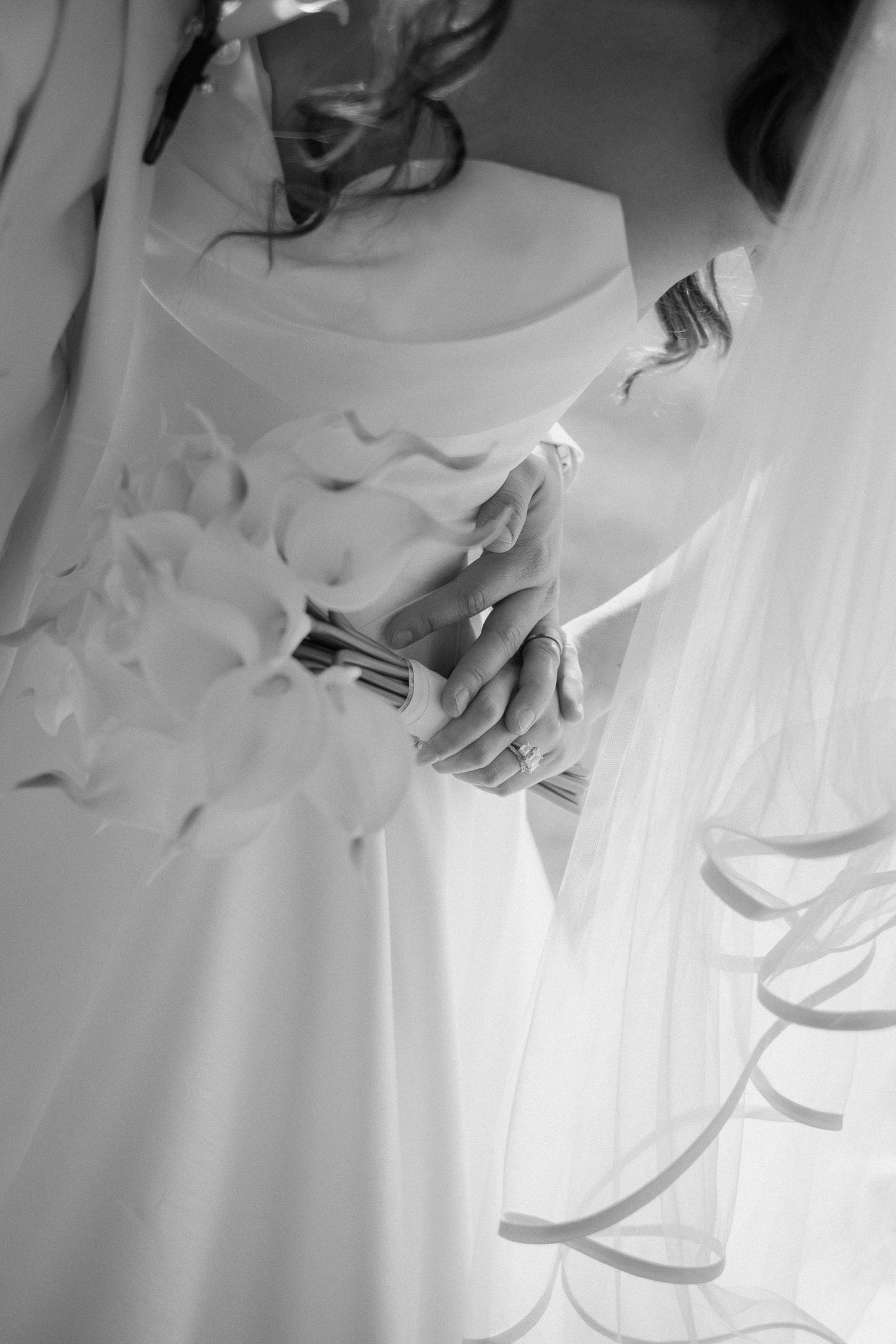 Black and white close-up of bride holding white calla lily bouquet in elegant wedding gown with flowing veil.