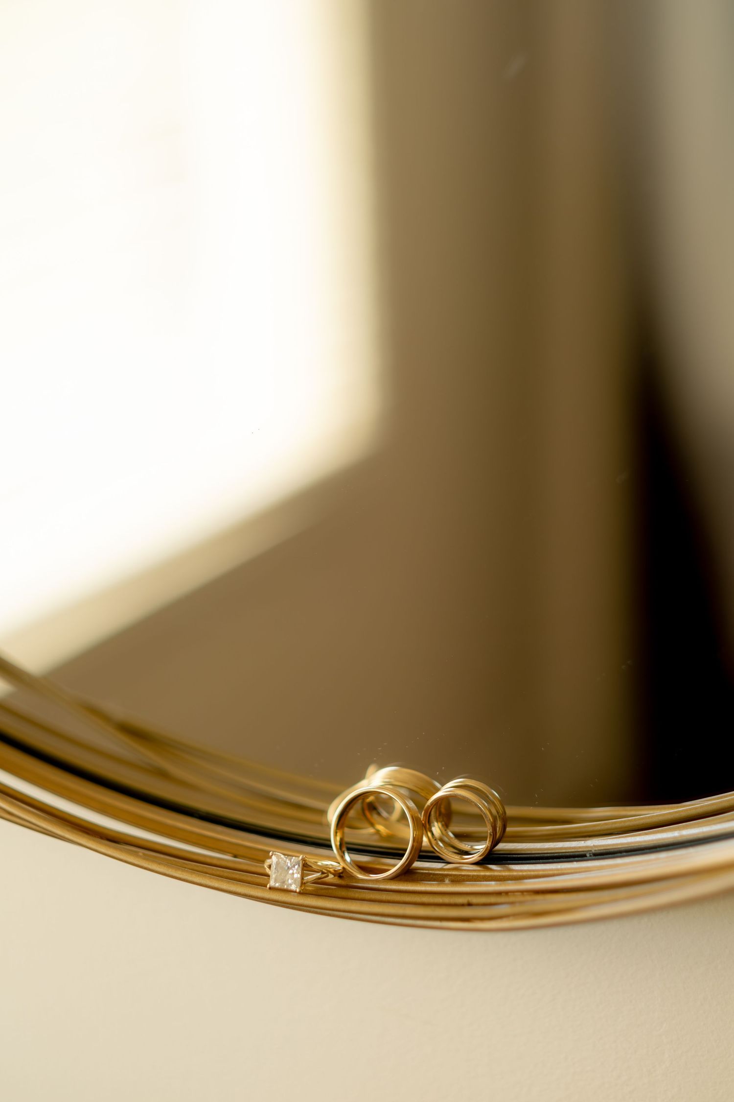 Gold wedding bands and diamond engagement ring resting on elegant golden mirror frame.