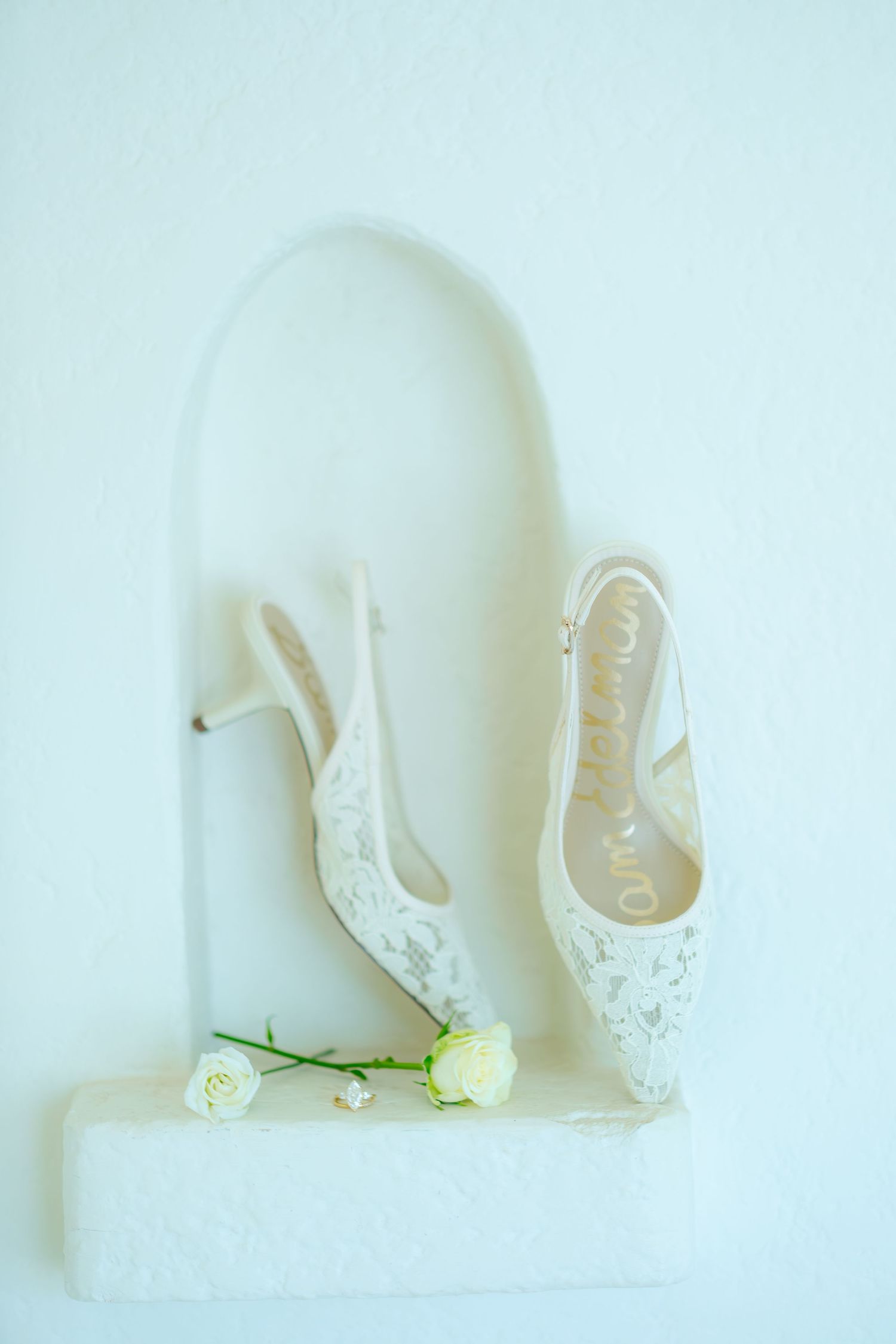 Elegant white lace Sam Edelman bridal heels displayed with a small rose on a white surface.