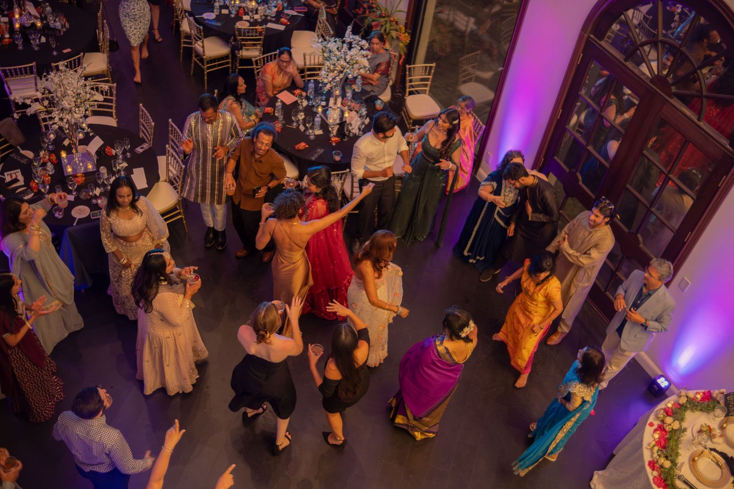 Guests dance and celebrate at a vibrant Indian fusion wedding reception with purple ambient lighting.