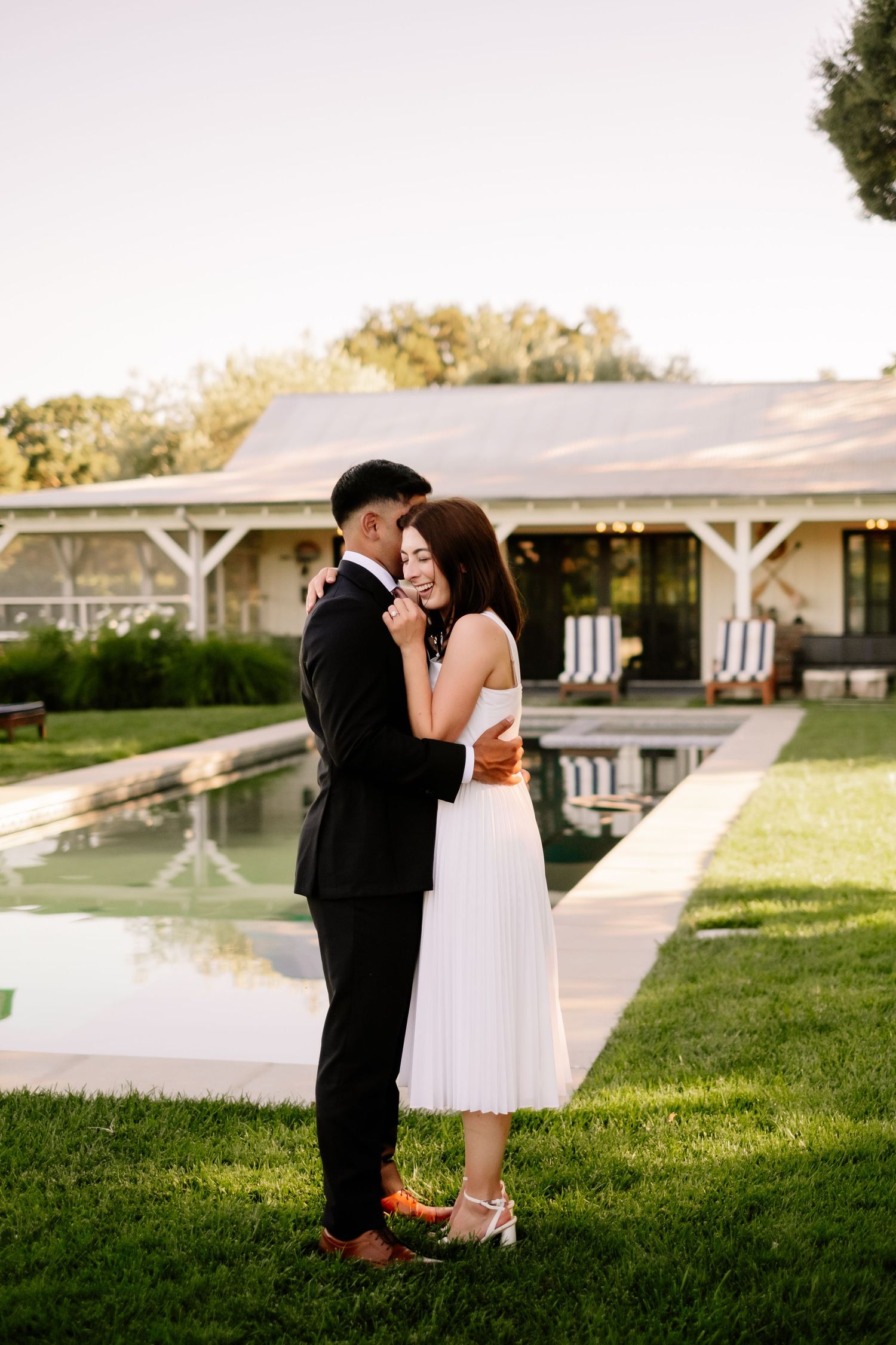 Couple sharing an intimate embrace on green lawn at golden hour near a pool.
