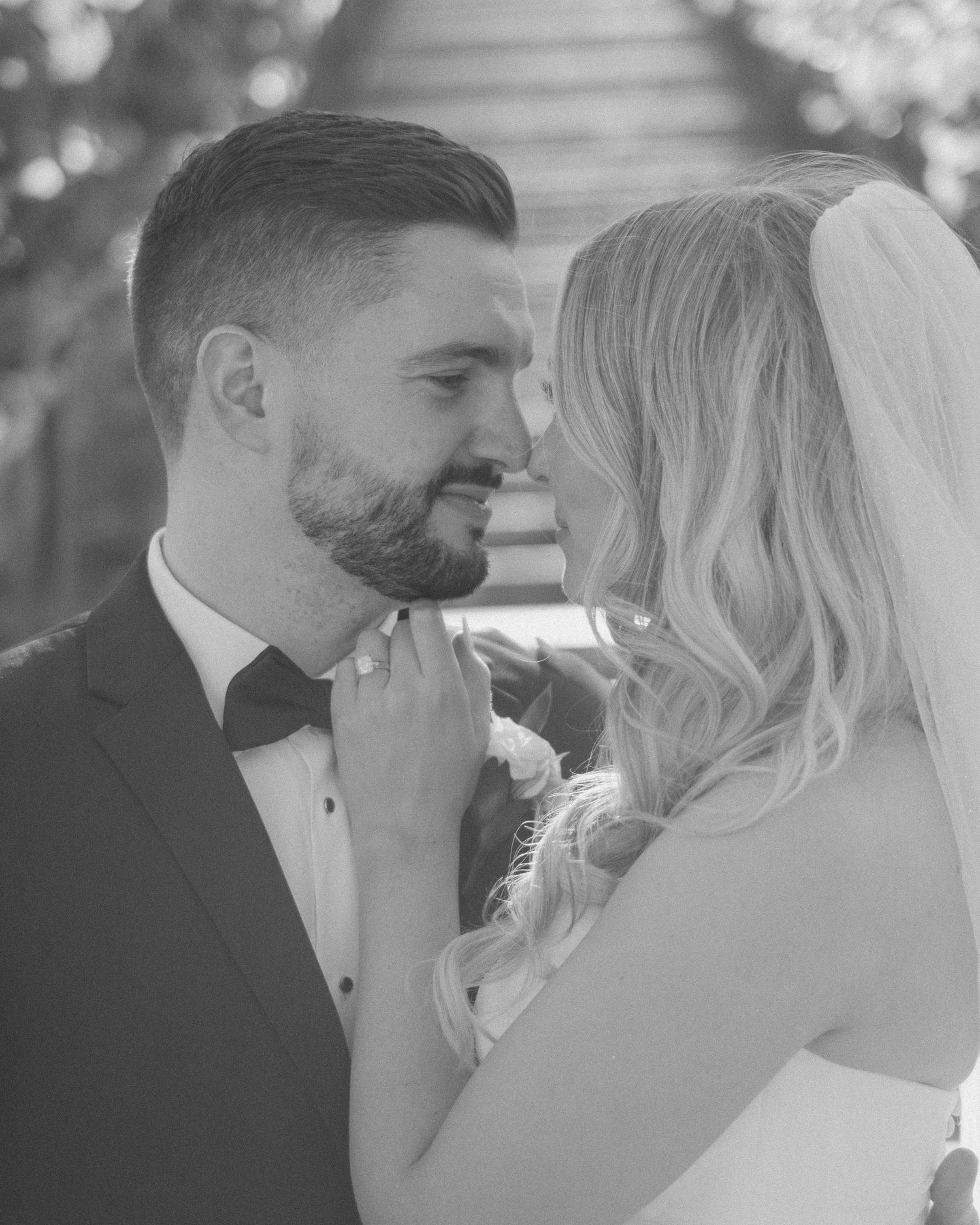 Black and white romantic close-up of bride and groom nearly kissing at outdoor wedding ceremony.