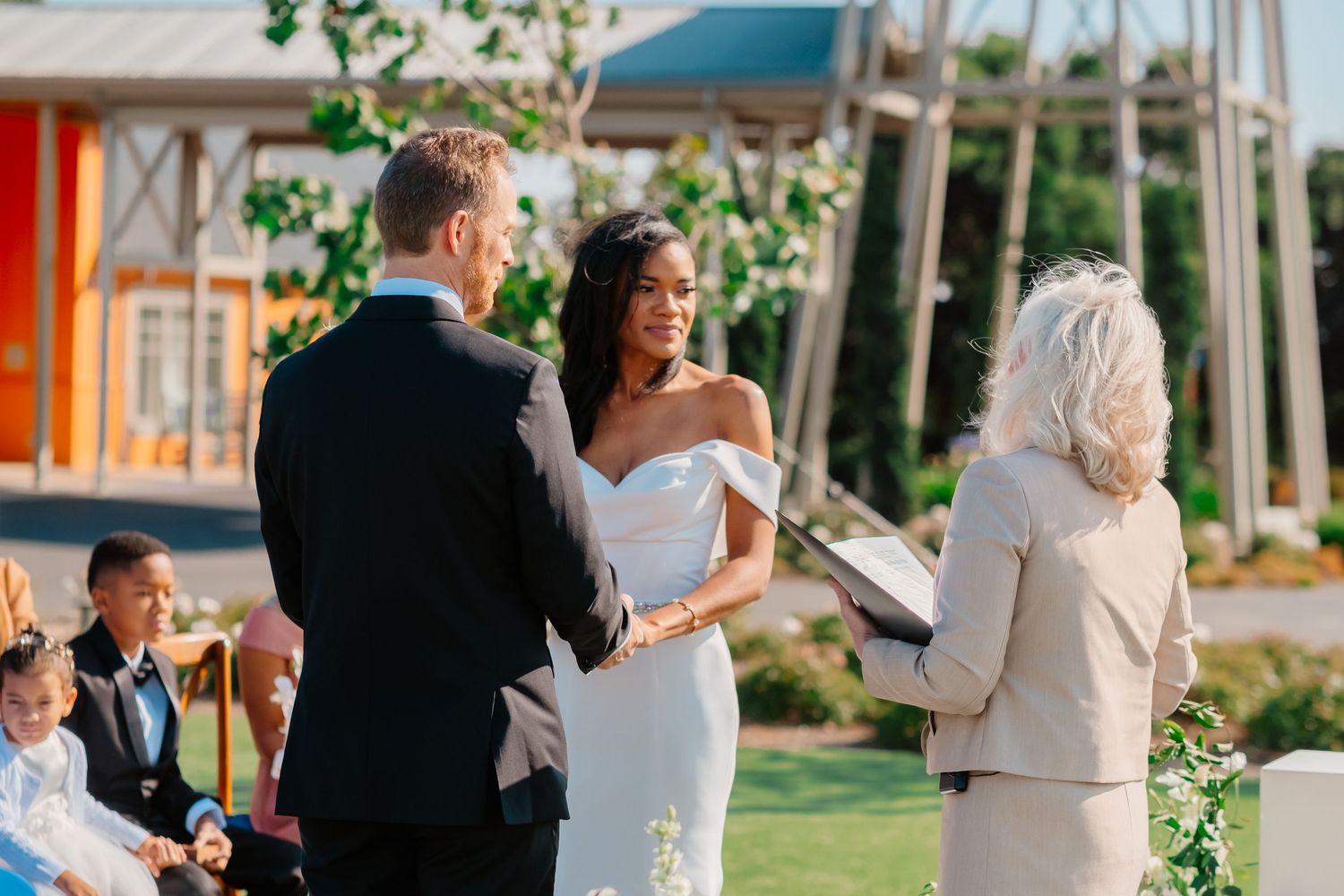Bride and groom exchange vows at outdoor wedding ceremony with officiant holding book.