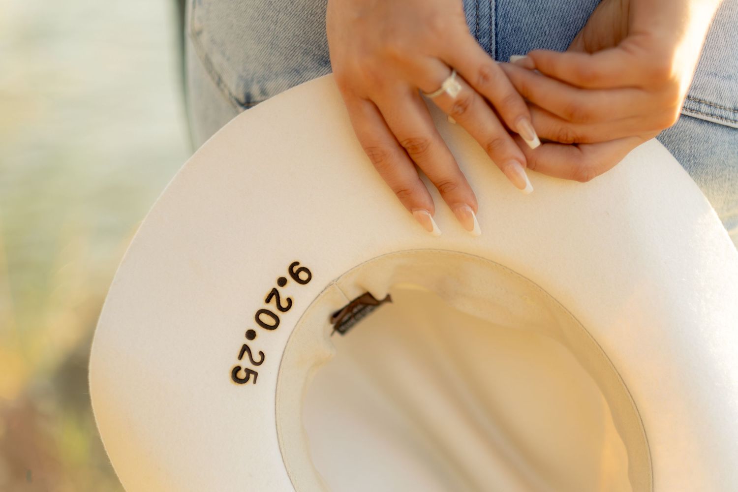 Close-up of hands holding a white cowboy hat with the date 9.20.25 burned into the brim.