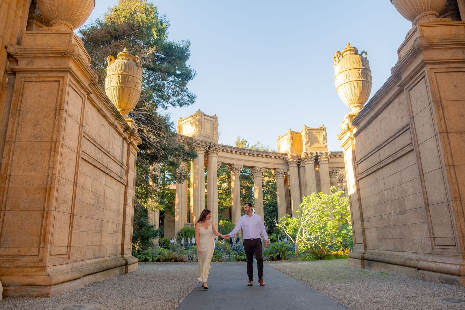 Couple walking hand in hand through grand columns at the Palace of Fine Arts in San Francisco.