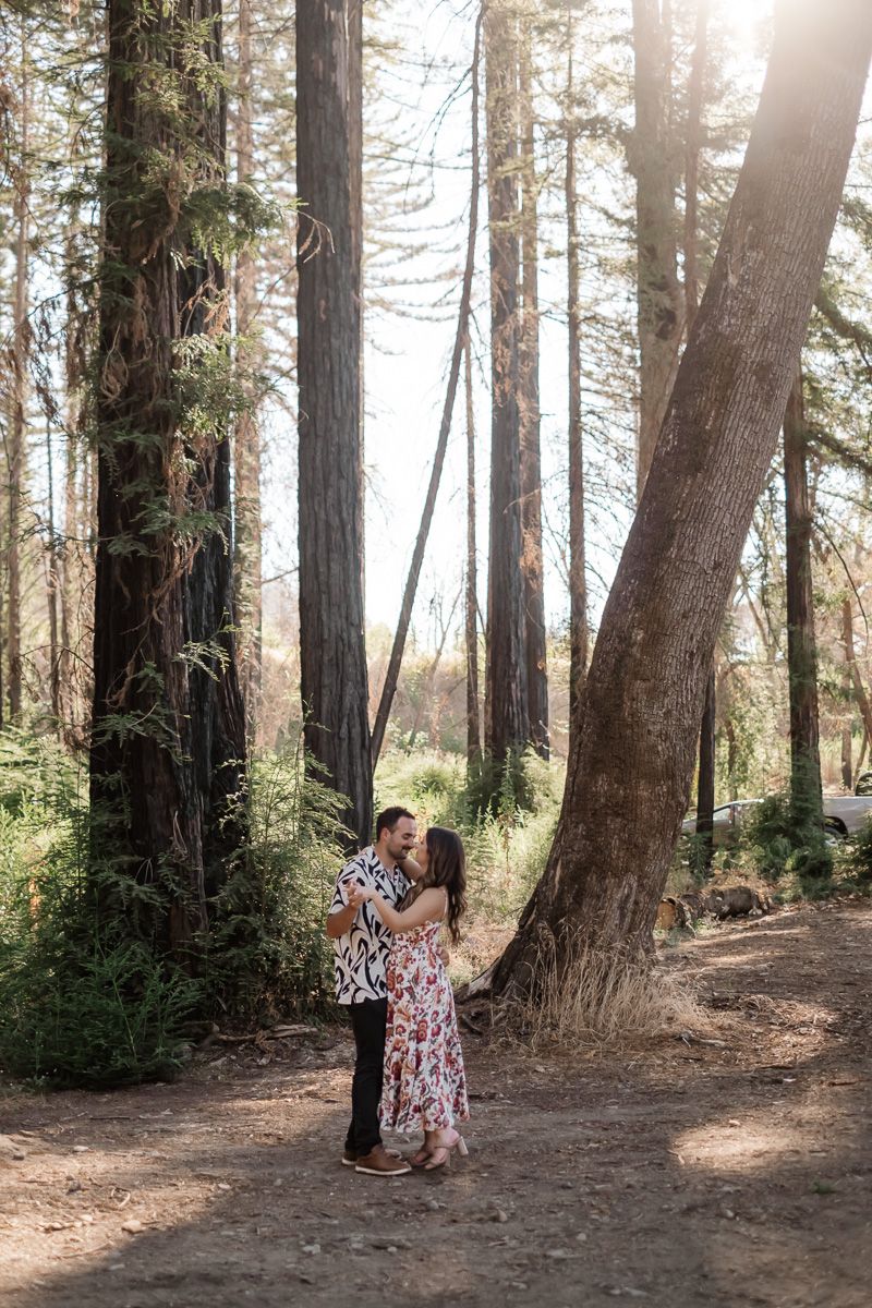 Couple kissing and embracing on a forest path surrounded by tall redwood trees.