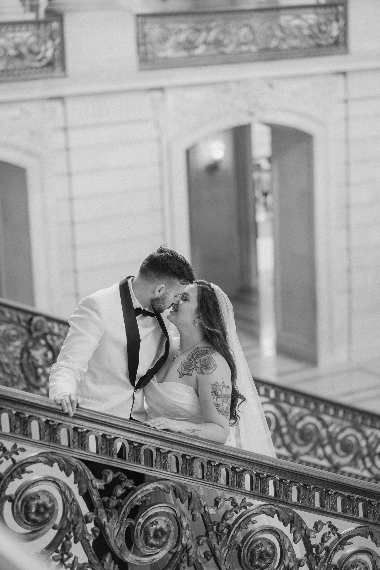 Bride and groom sharing a romantic kiss on ornate balcony railing in black and white.
