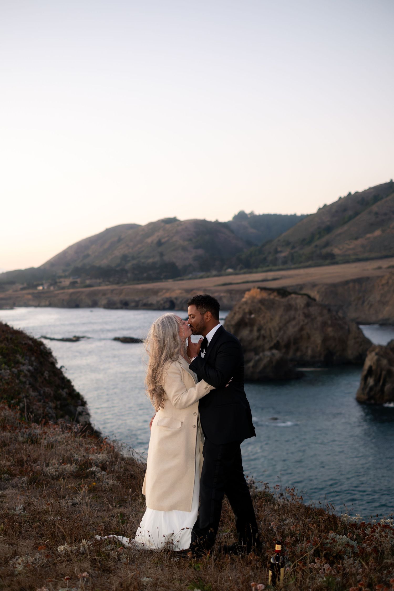 Couple sharing a romantic kiss at sunset overlooking the scenic California coastline during their wedding elopement.