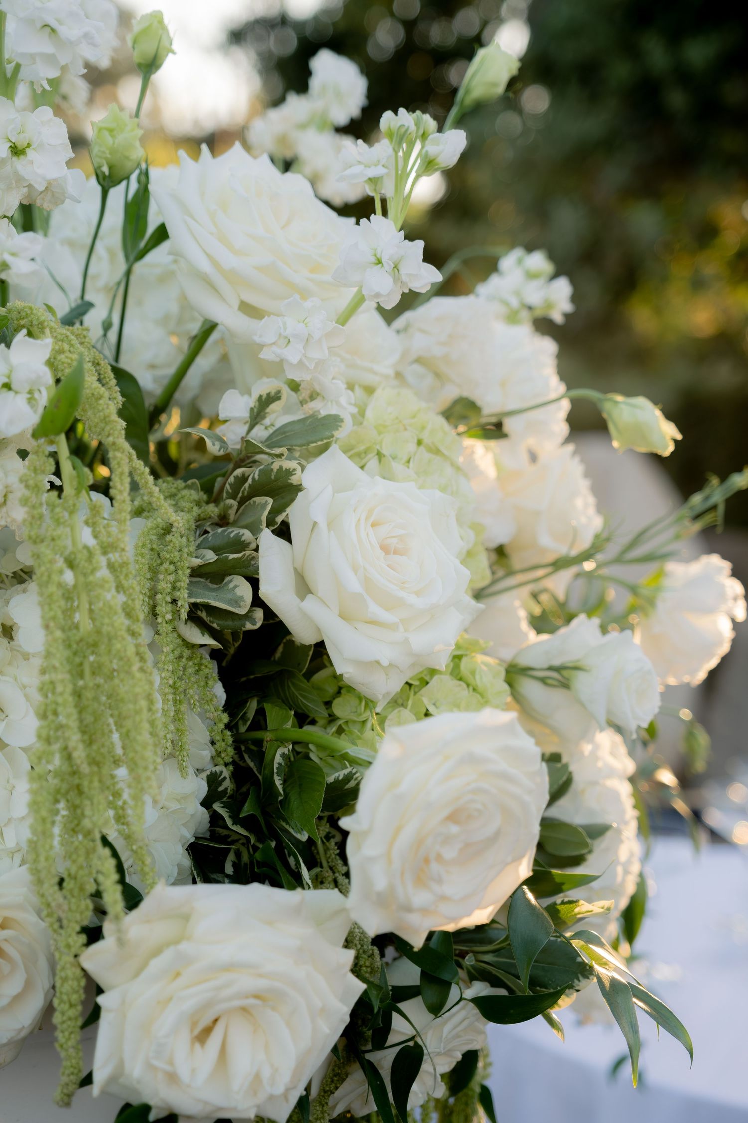 Close-up of elegant wedding floral arrangement featuring white roses, hydrangeas, and cascading green amaranthus.