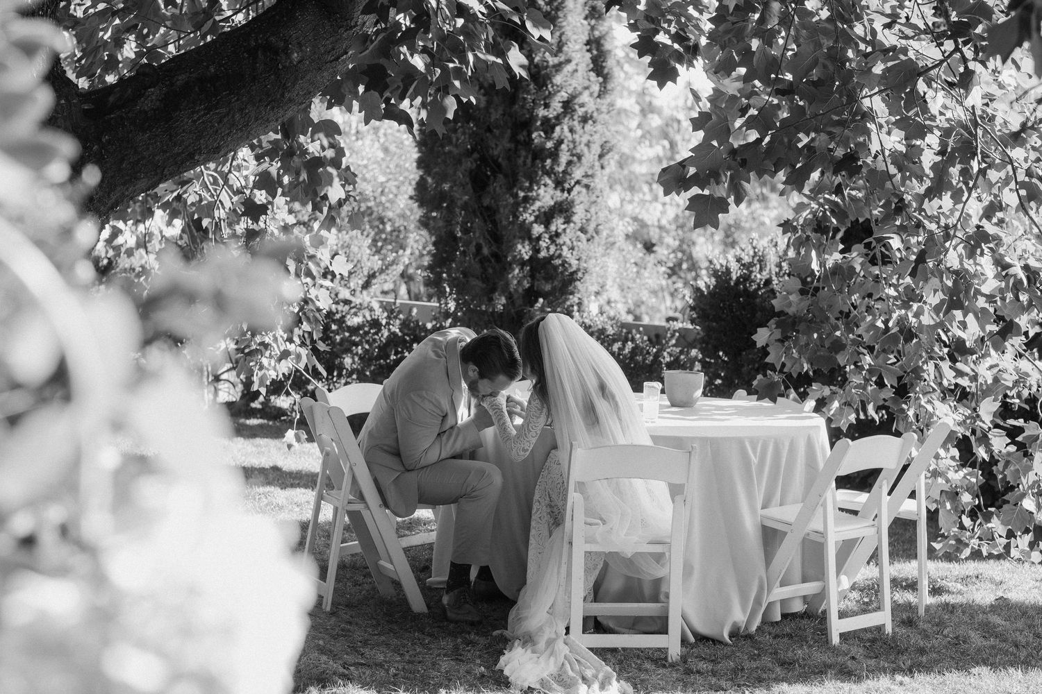 Black and white photo of bride and groom sharing intimate moment at outdoor garden wedding table.