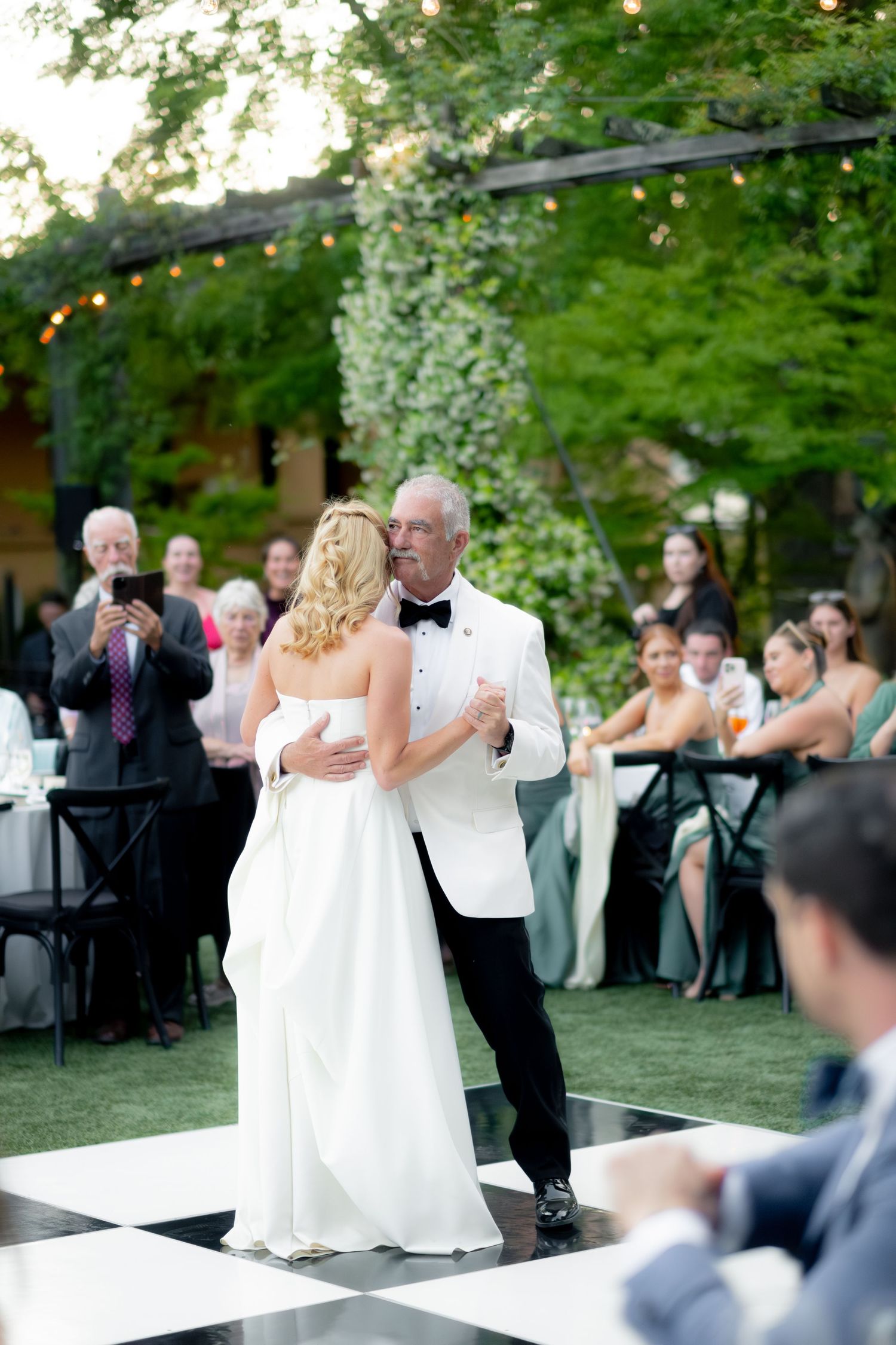 Bride and her father sharing a father-daughter dance on a black and white checkered dance floor outdoors.