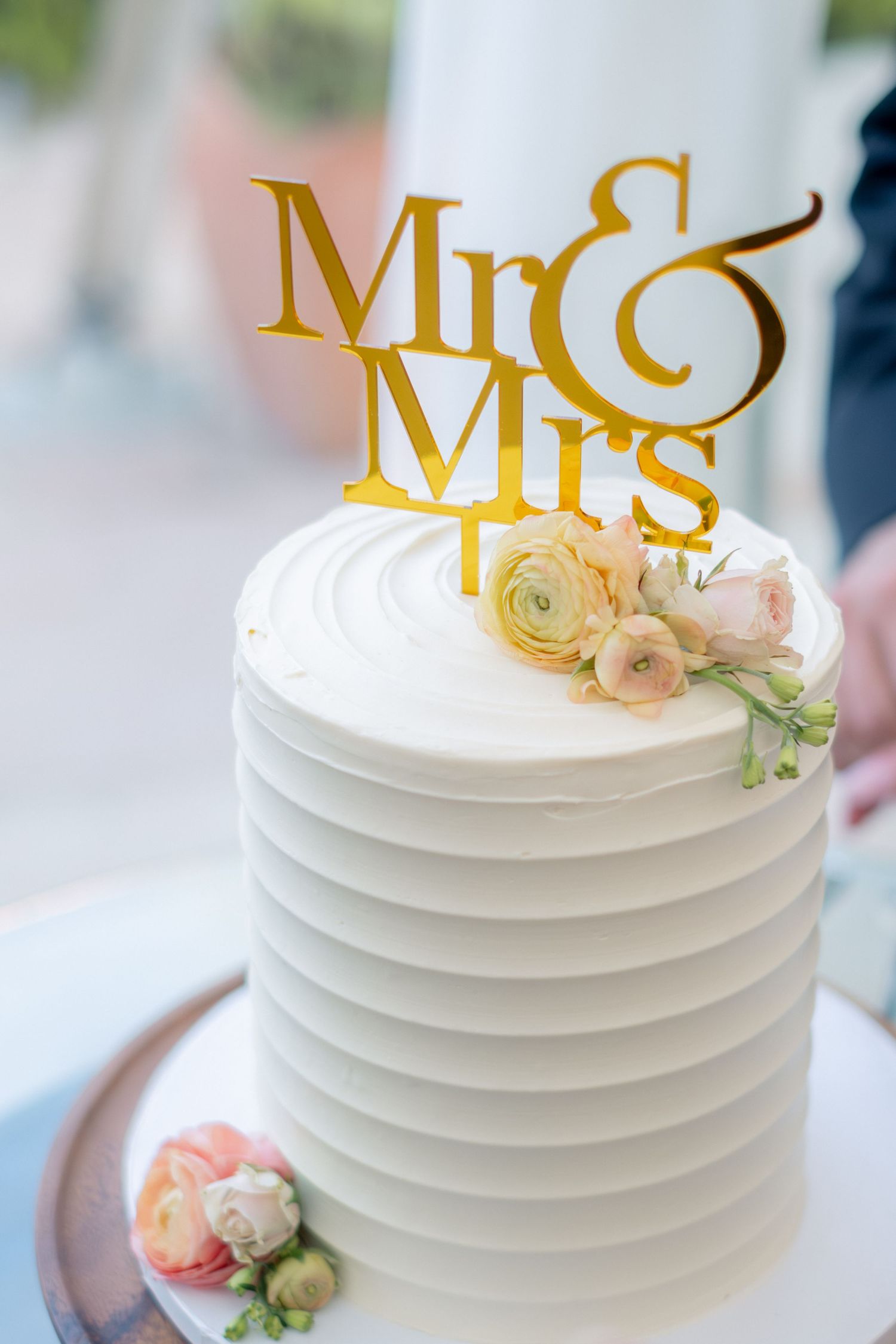 Elegant single-tier white wedding cake with gold Mr and Mrs topper and peach floral accents.