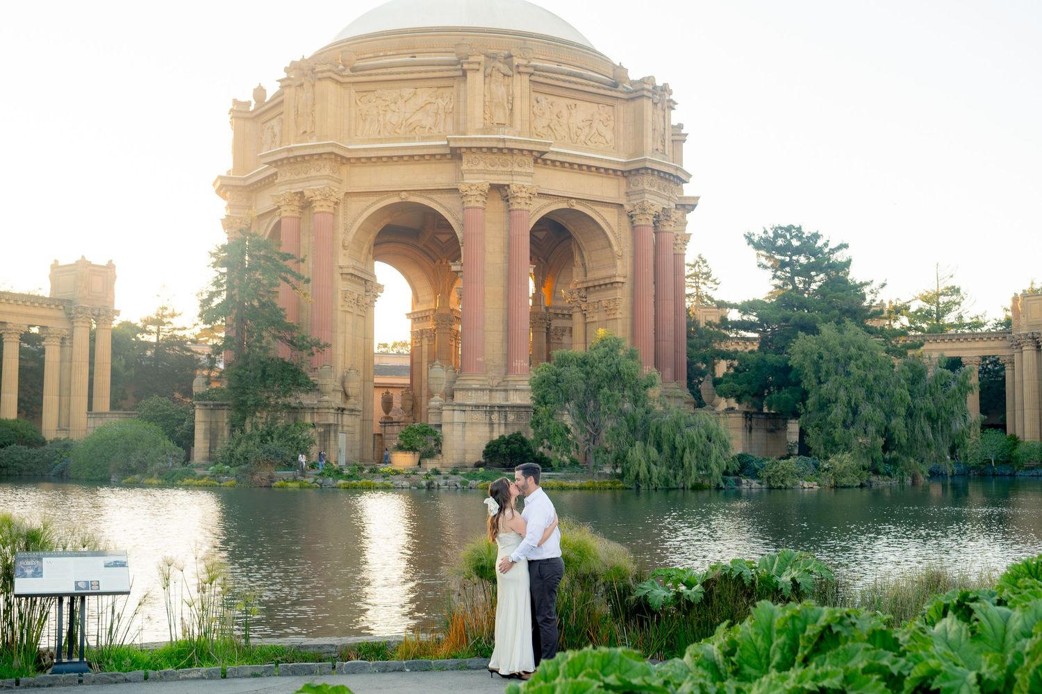 Engaged couple embracing in front of the Palace of Fine Arts rotunda at golden hour.