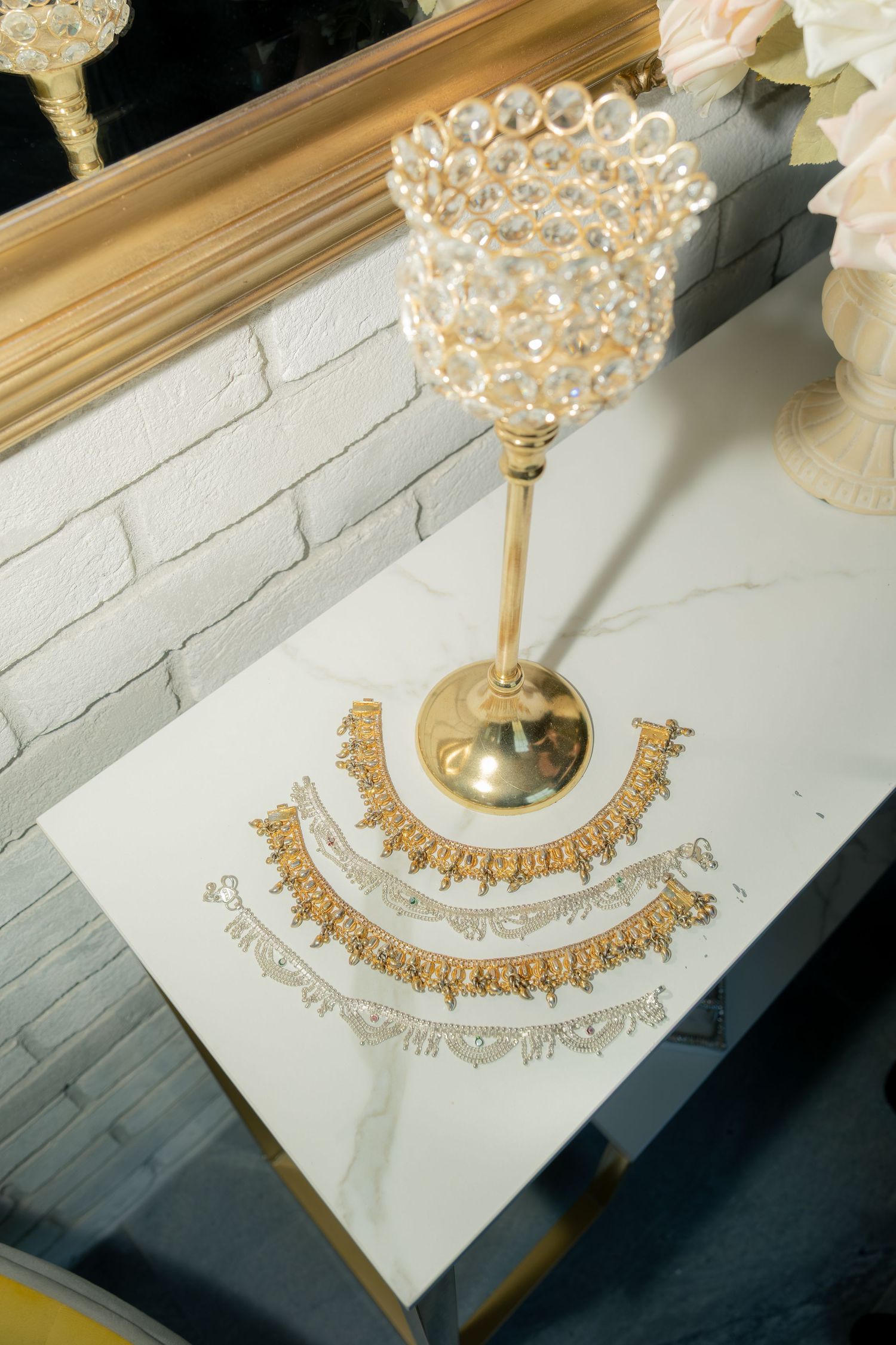 Gold bridal jewelry necklaces displayed on white marble table with crystal candleholder.