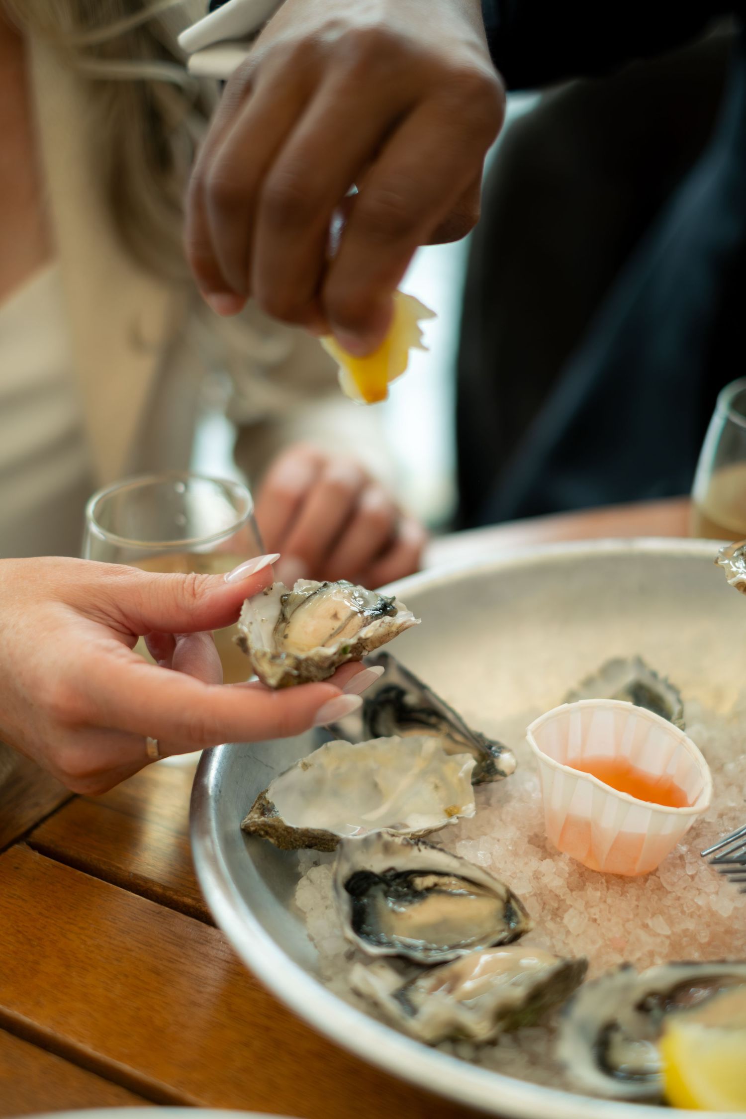 Hands holding fresh oysters on ice with cocktail sauce and lemon at an elegant seafood dining experience.