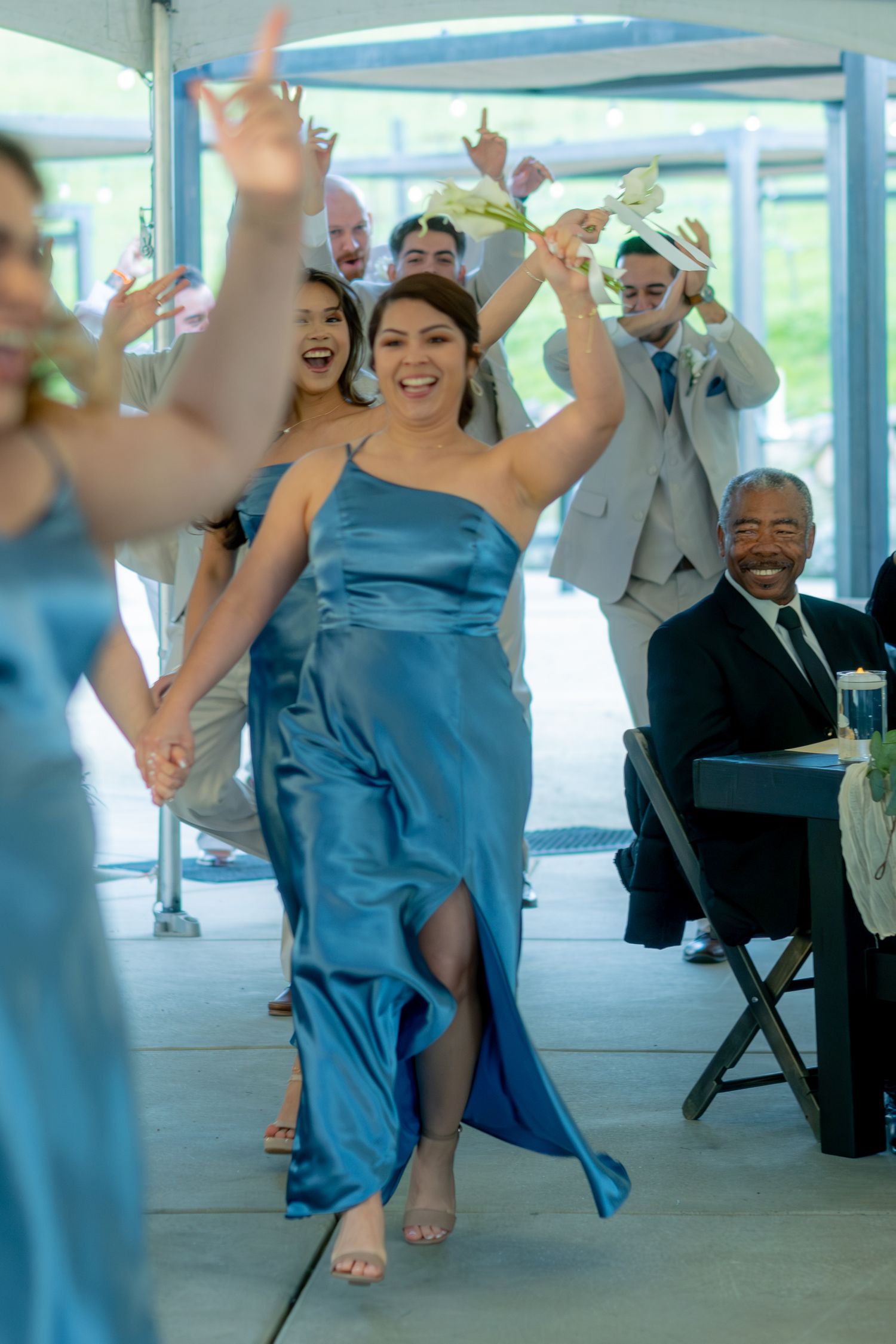 Bridesmaid in blue satin one-shoulder gown dancing joyfully during wedding reception grand entrance.