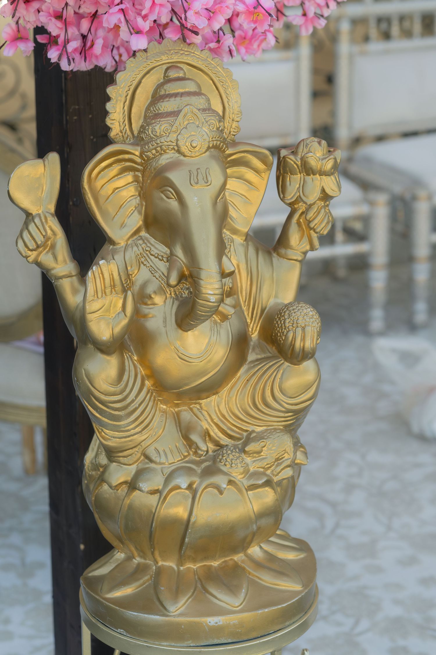 Golden Ganesha statue seated on lotus with pink flowers in background at wedding venue.