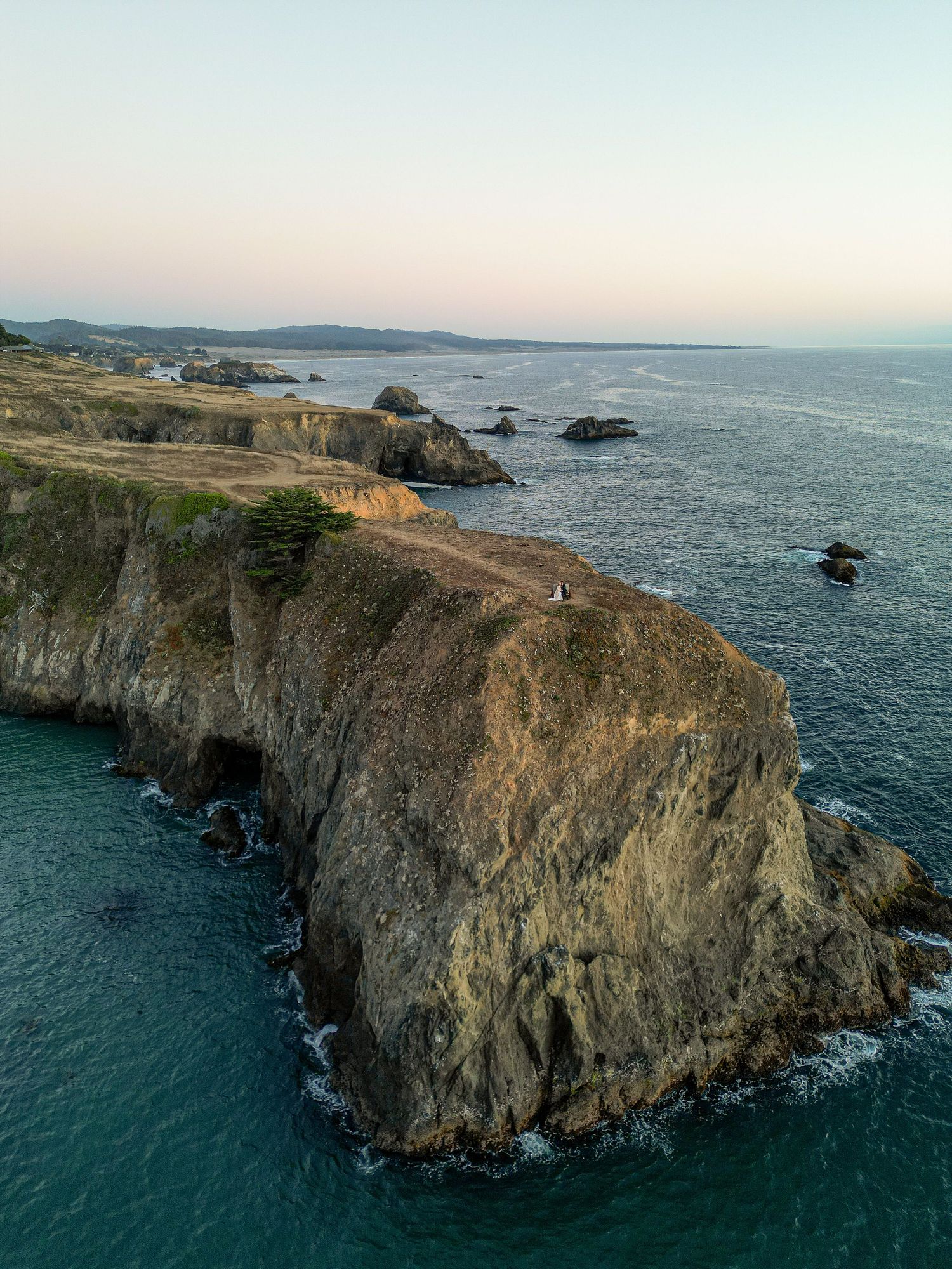 Aerial drone view of rugged coastal cliffs overlooking turquoise ocean waters at sunset.