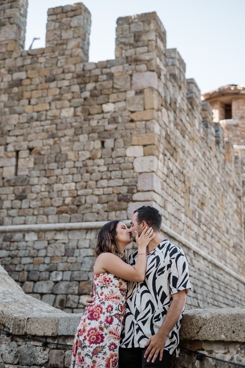Couple sharing a romantic kiss in front of an ancient stone castle wall.