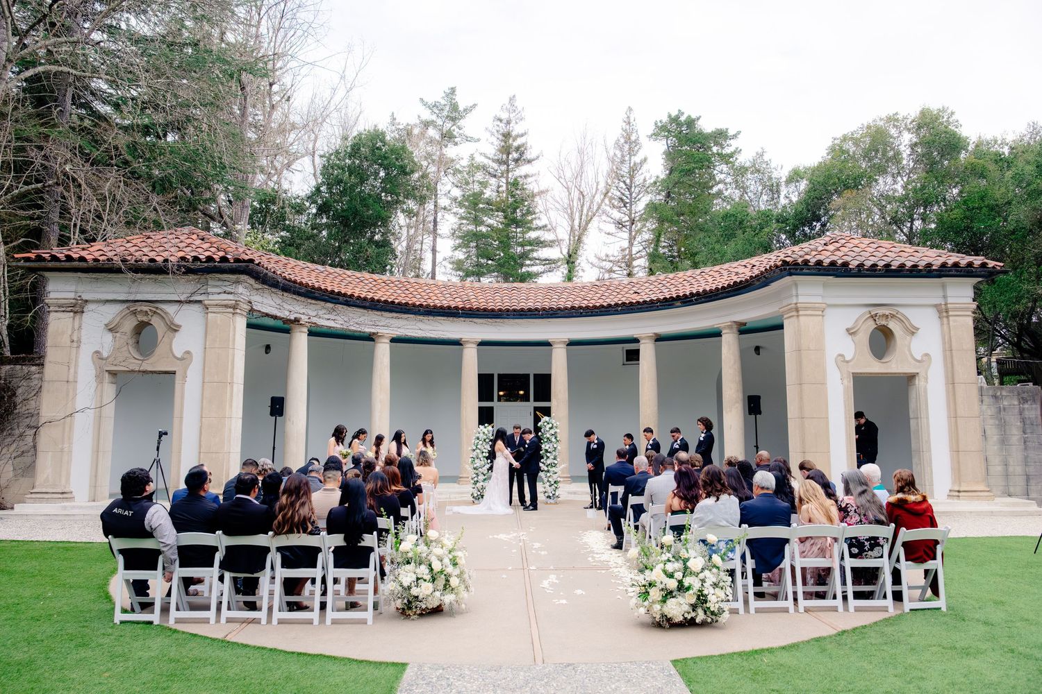 Outdoor wedding ceremony at an elegant venue with white chairs and floral arrangements.