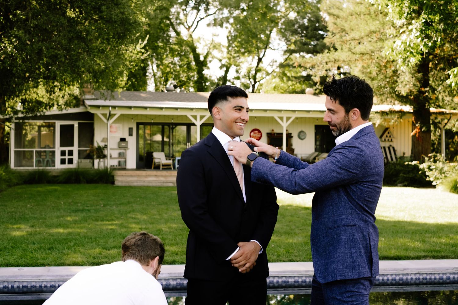 Groomsmen adjusting neckties in a lush garden setting before a wedding ceremony.