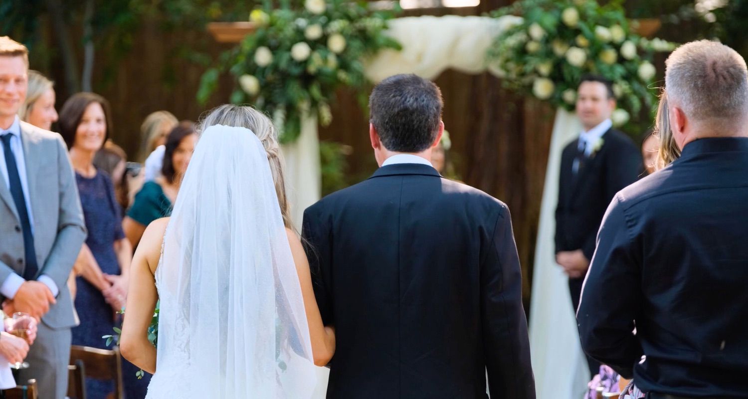Bride and groom standing at the altar during an outdoor wedding ceremony surrounded by guests and lush greenery.