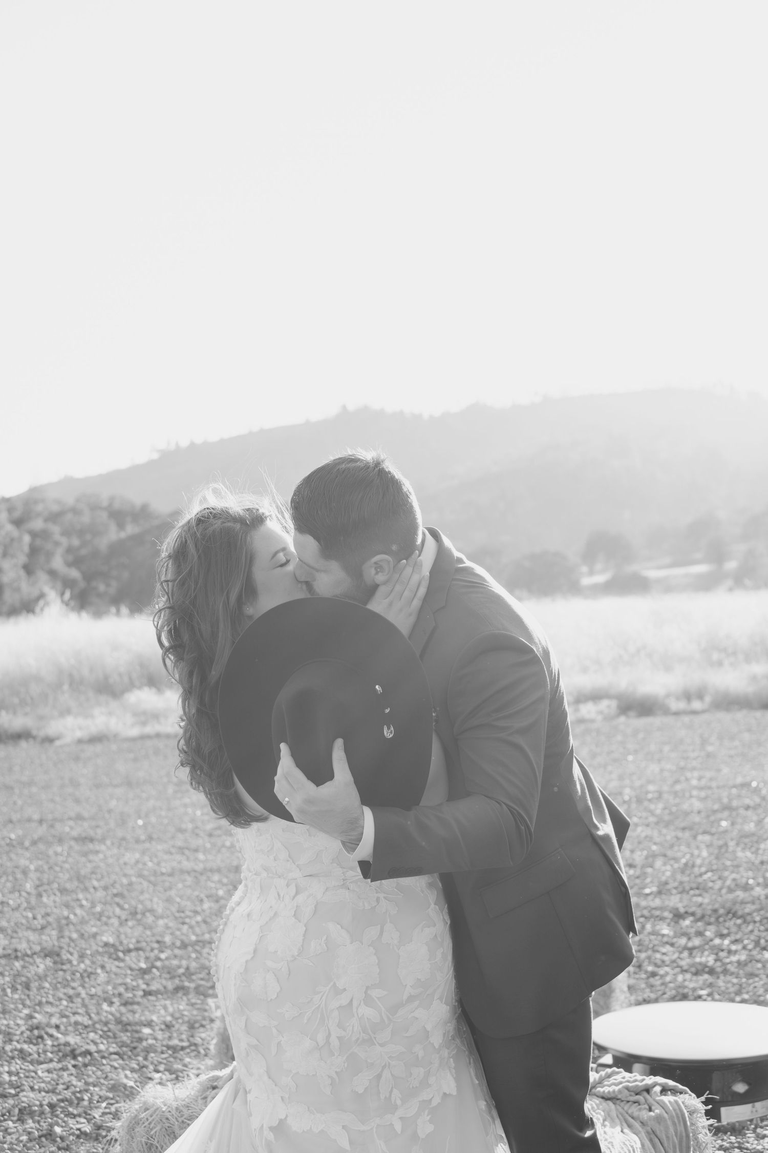 Black and white photo of bride and groom sharing a kiss in open field.